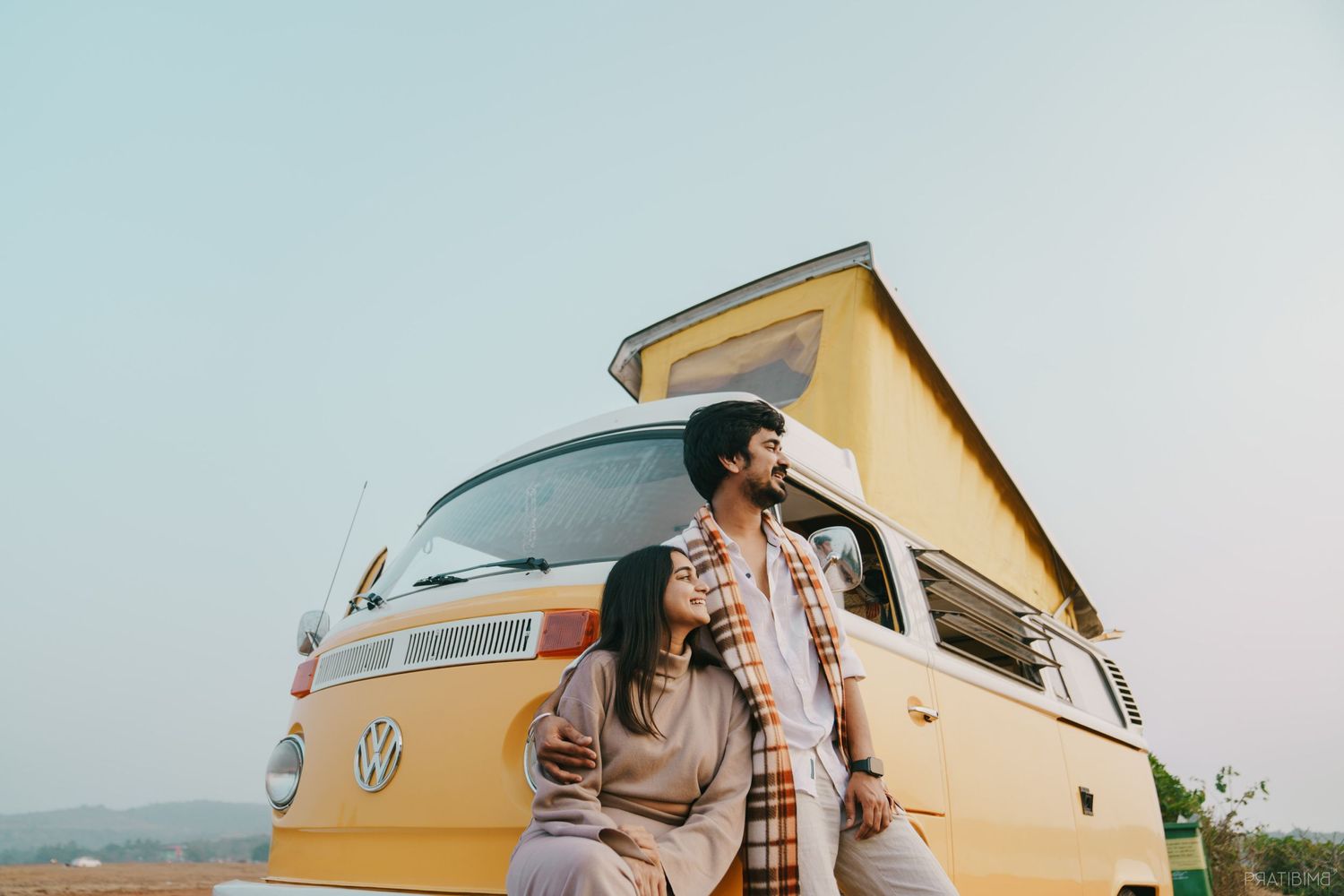 Couple sharing intimate moments near a vintage yellow Volkswagen van.