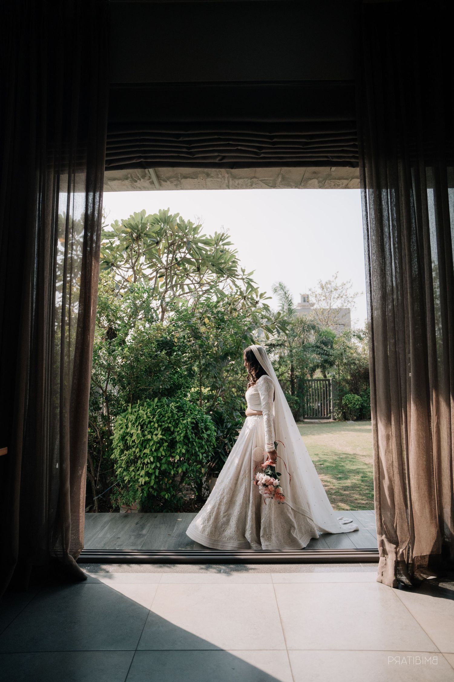 Silhouette of bride in flowing gown framed by doorway with garden view.