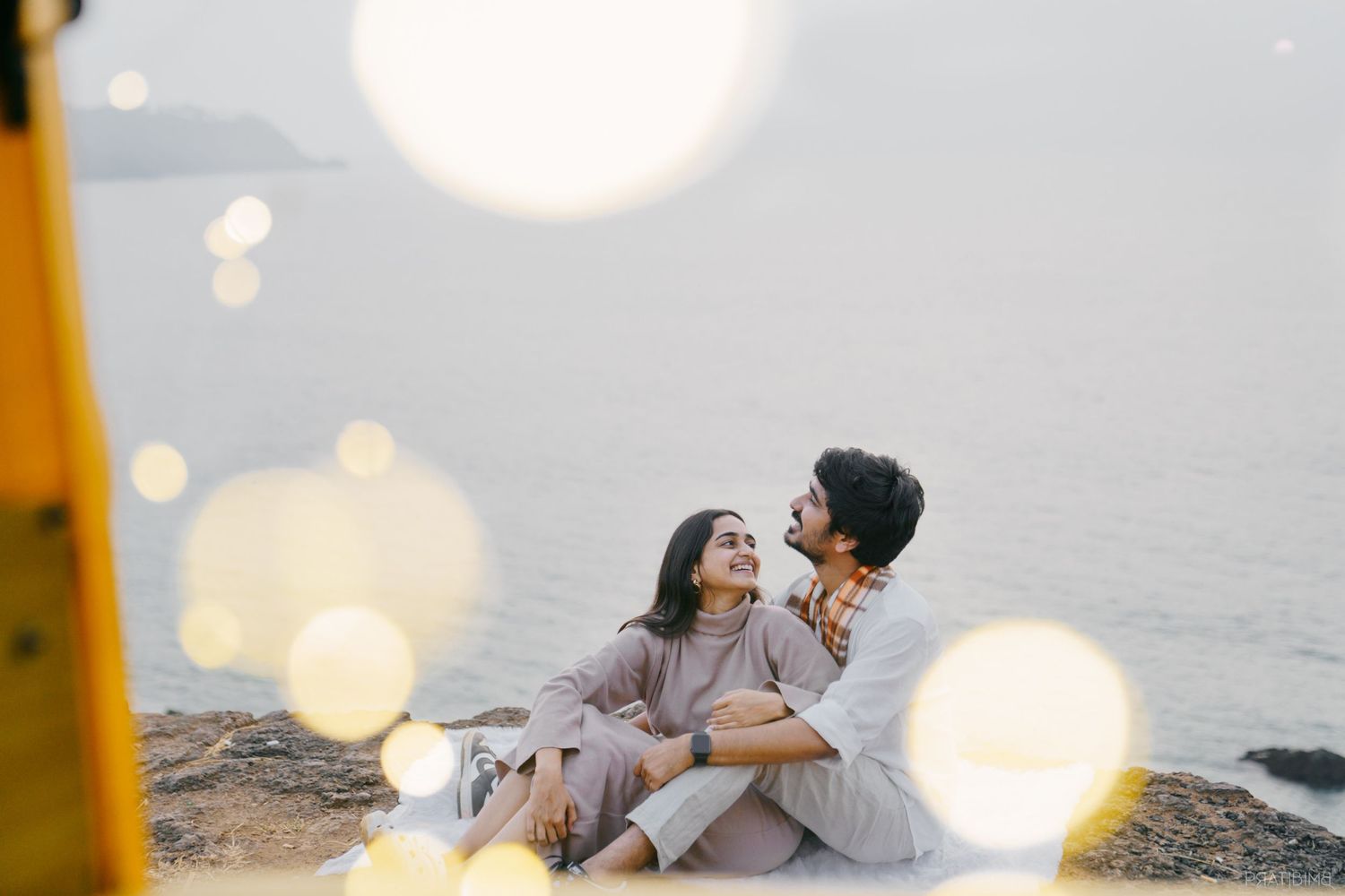 Romantic couple embracing by the water with dreamy bokeh lights in the background.