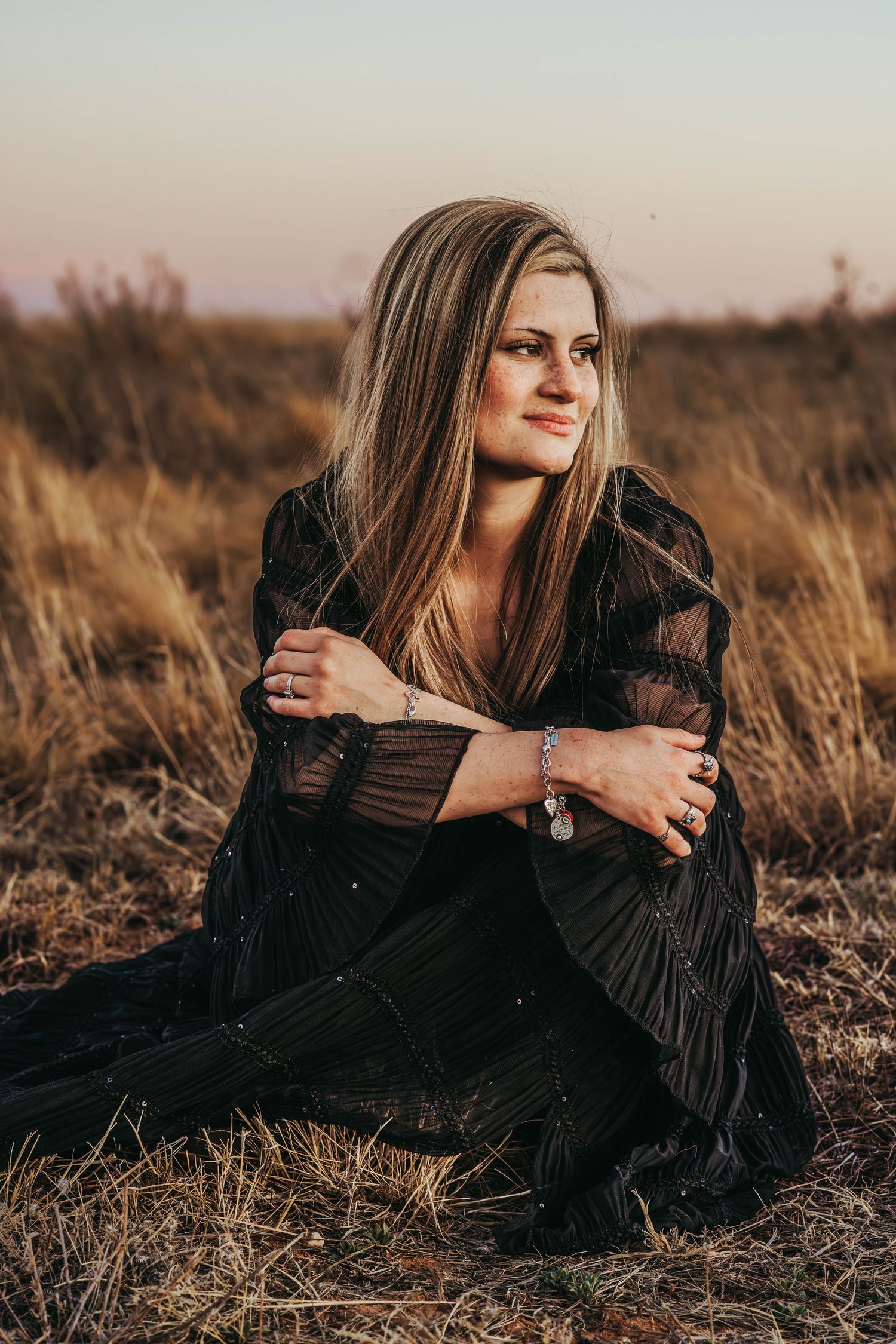 A person in a black dress lies in golden autumn grass during sunset creating a moody outdoor portrait.
