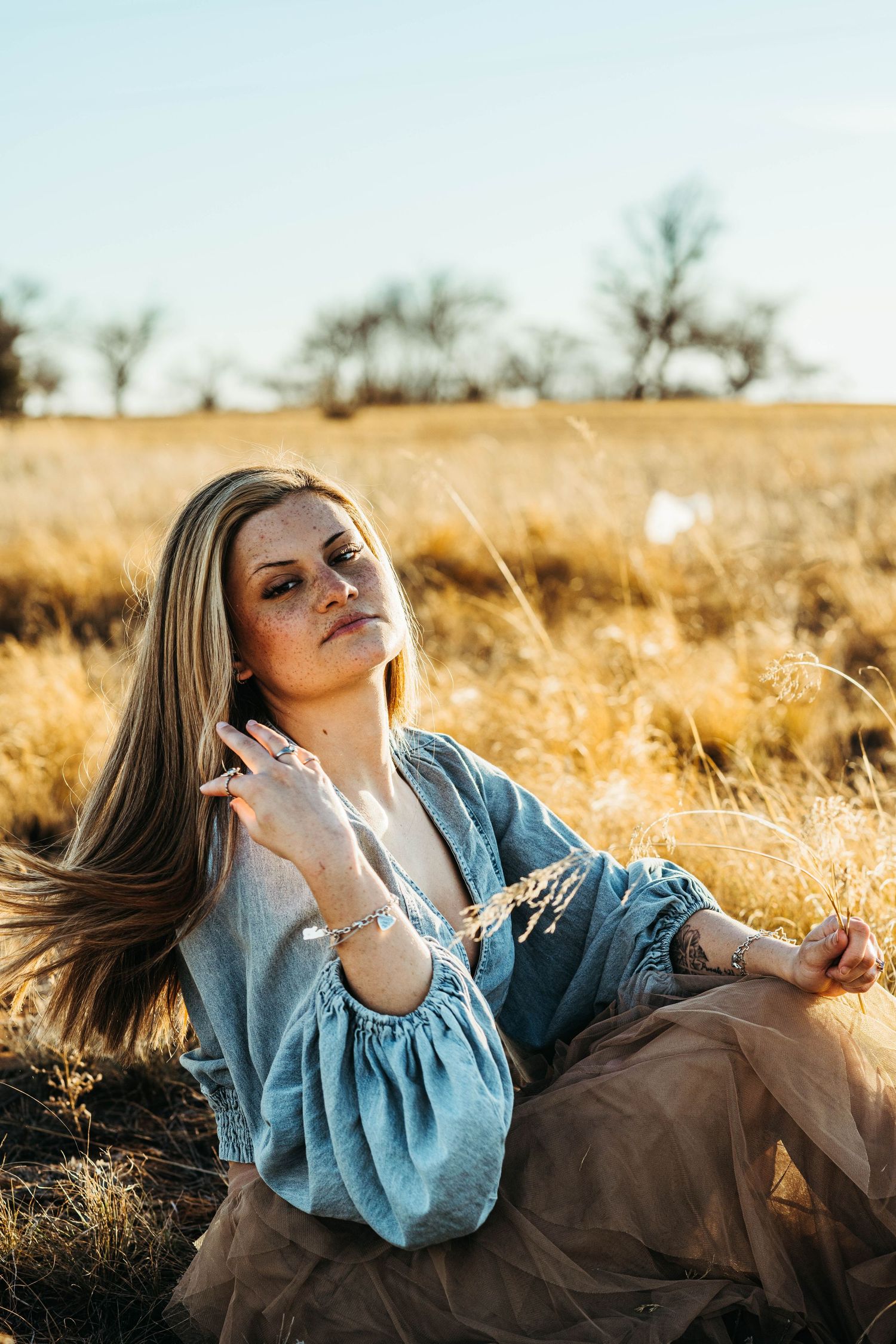 Woman in denim top and brown skirt poses gracefully in golden field during sunset photoshoot.