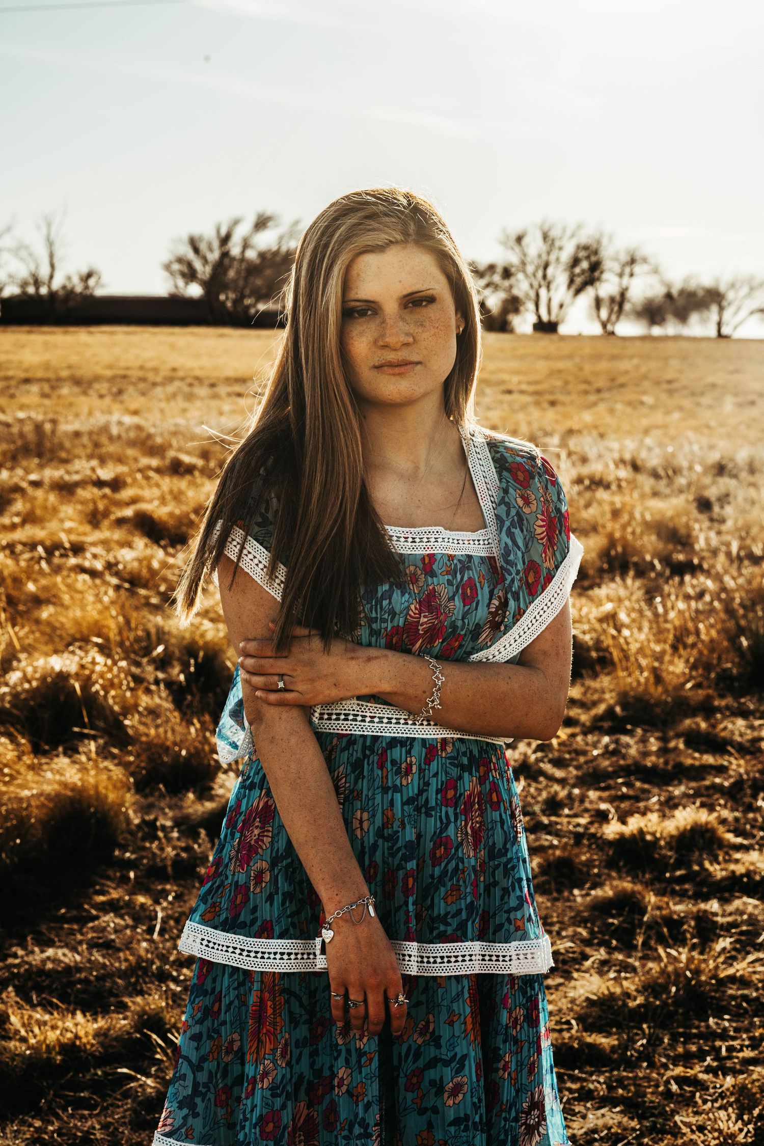 A series of golden hour portraits in a field showing a blue and turquoise patterned dress with white trim details.