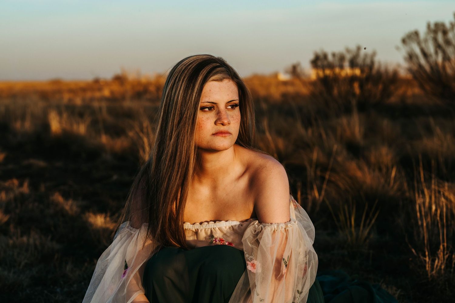 A person in a white lace dress poses against a golden sunset backdrop in a desert landscape.