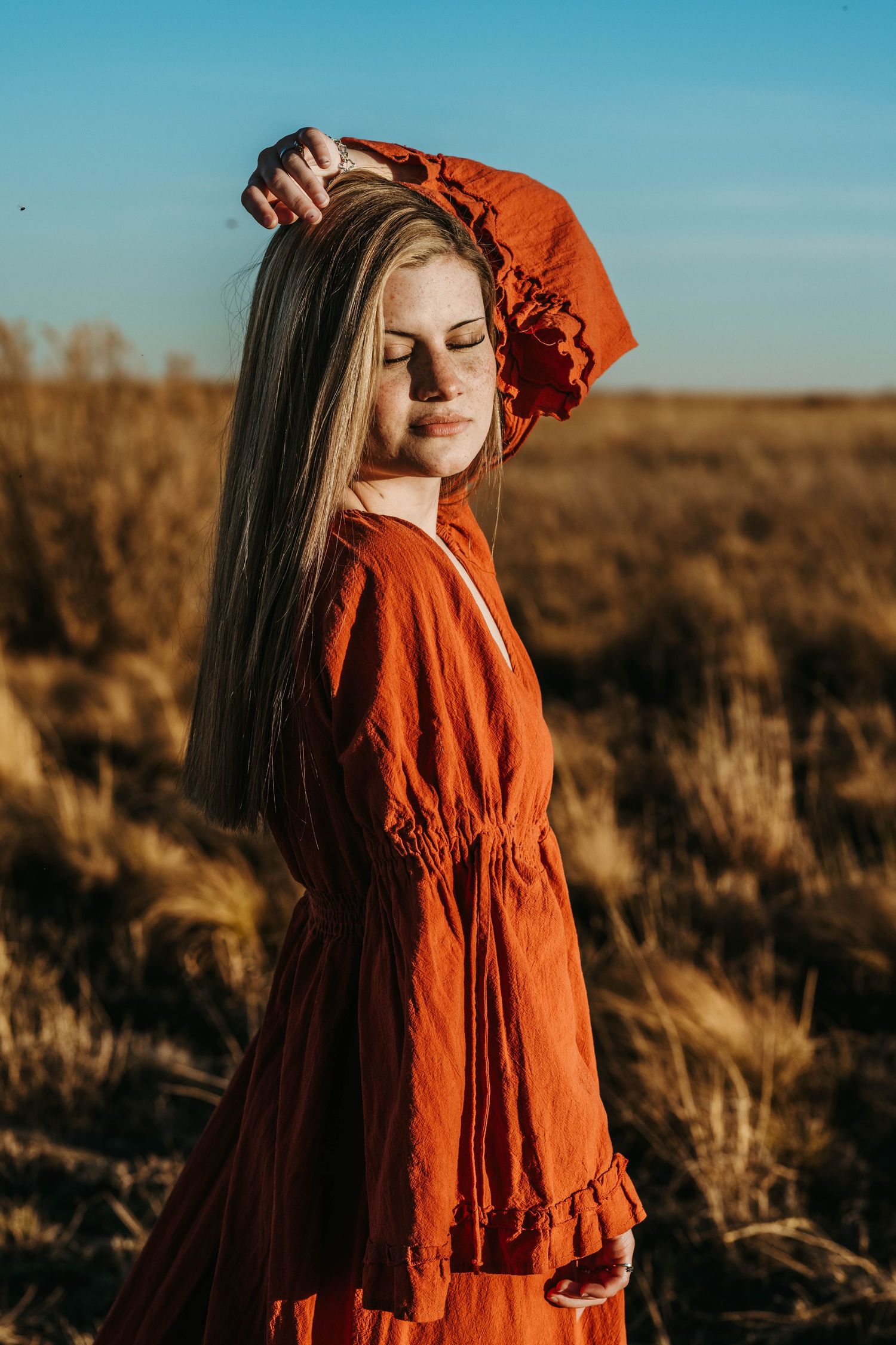 A series of sunset portraits in a field showing a person wearing a flowing rust-colored dress against golden light and dry brush.