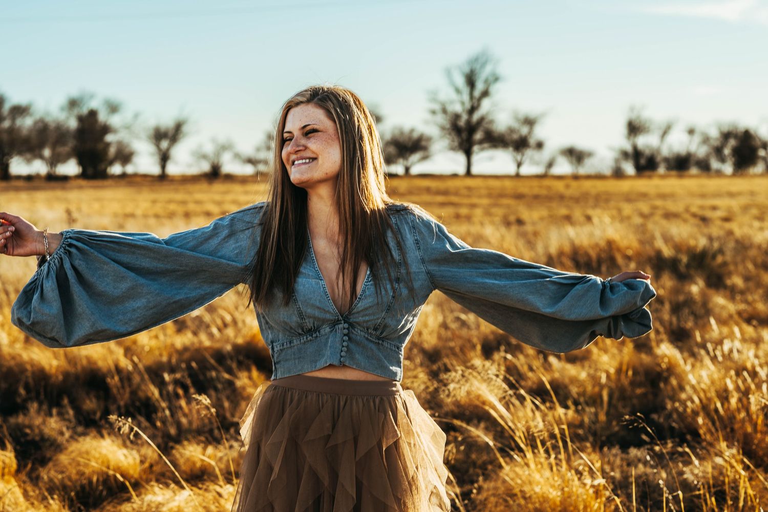 A person in a blue denim jacket spins joyfully in a golden wheat field at sunset.