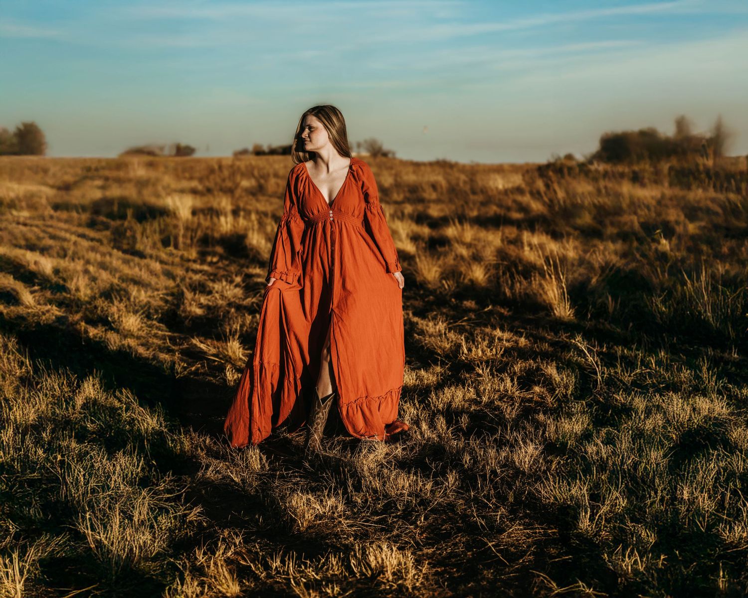 A person in a flowing red dress stands in a golden desert landscape at sunset with dramatic shadows.