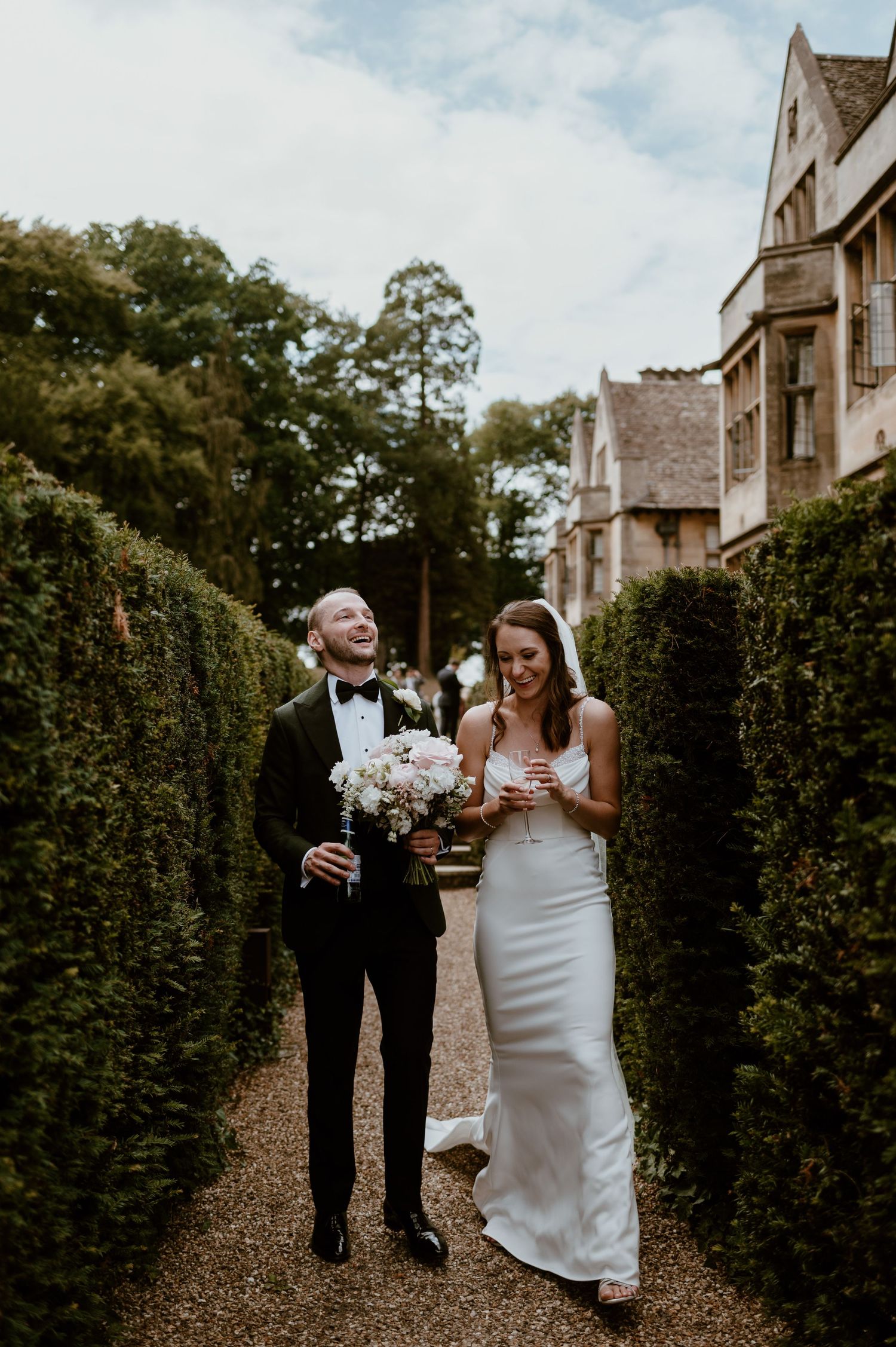 A couple shares joyful laughter while walking together through a garden path on their wedding day.