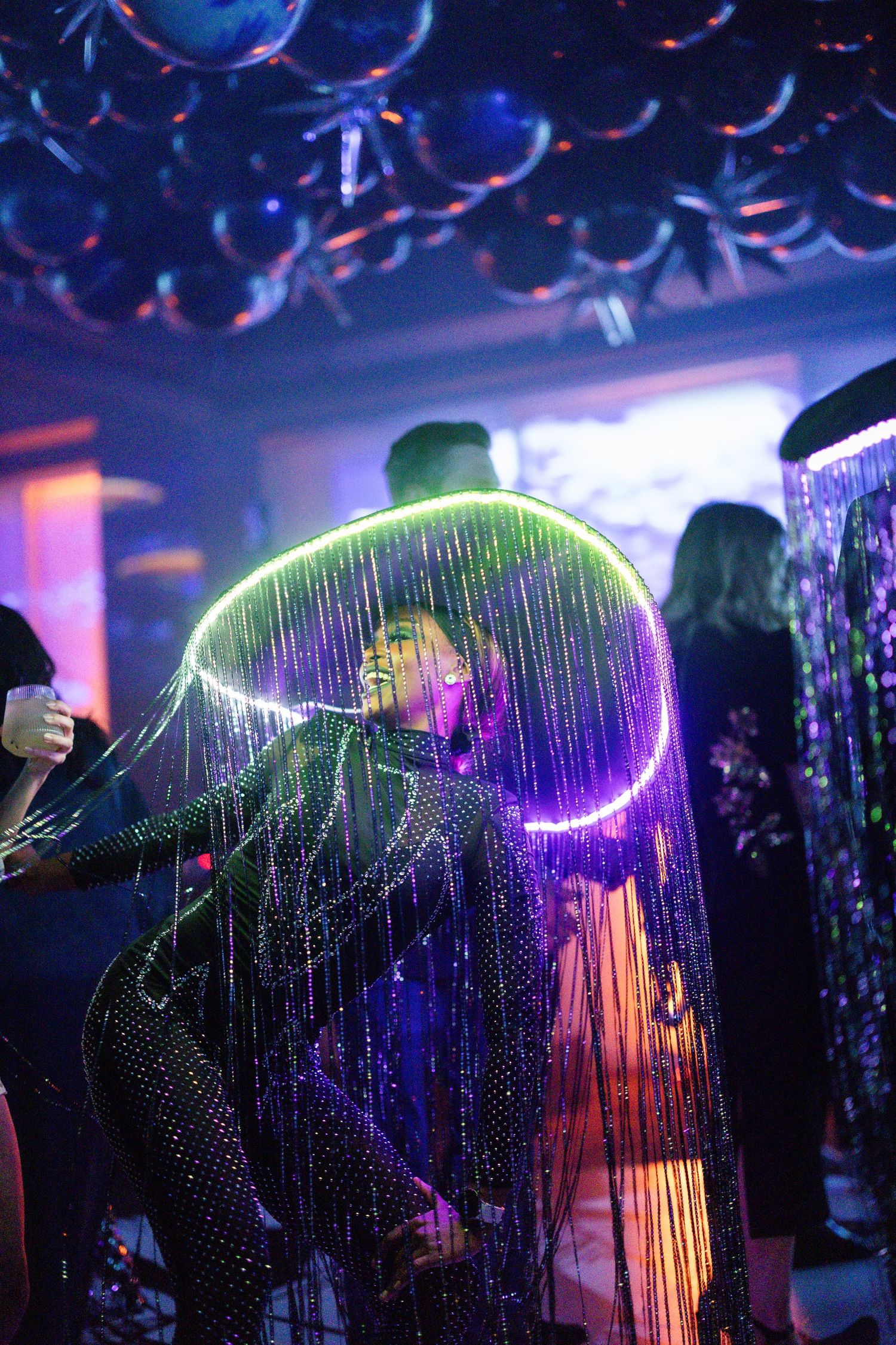 Illuminated fiber optic curtains create a mesmerizing light display in a dark nightclub setting with purple and blue hues.