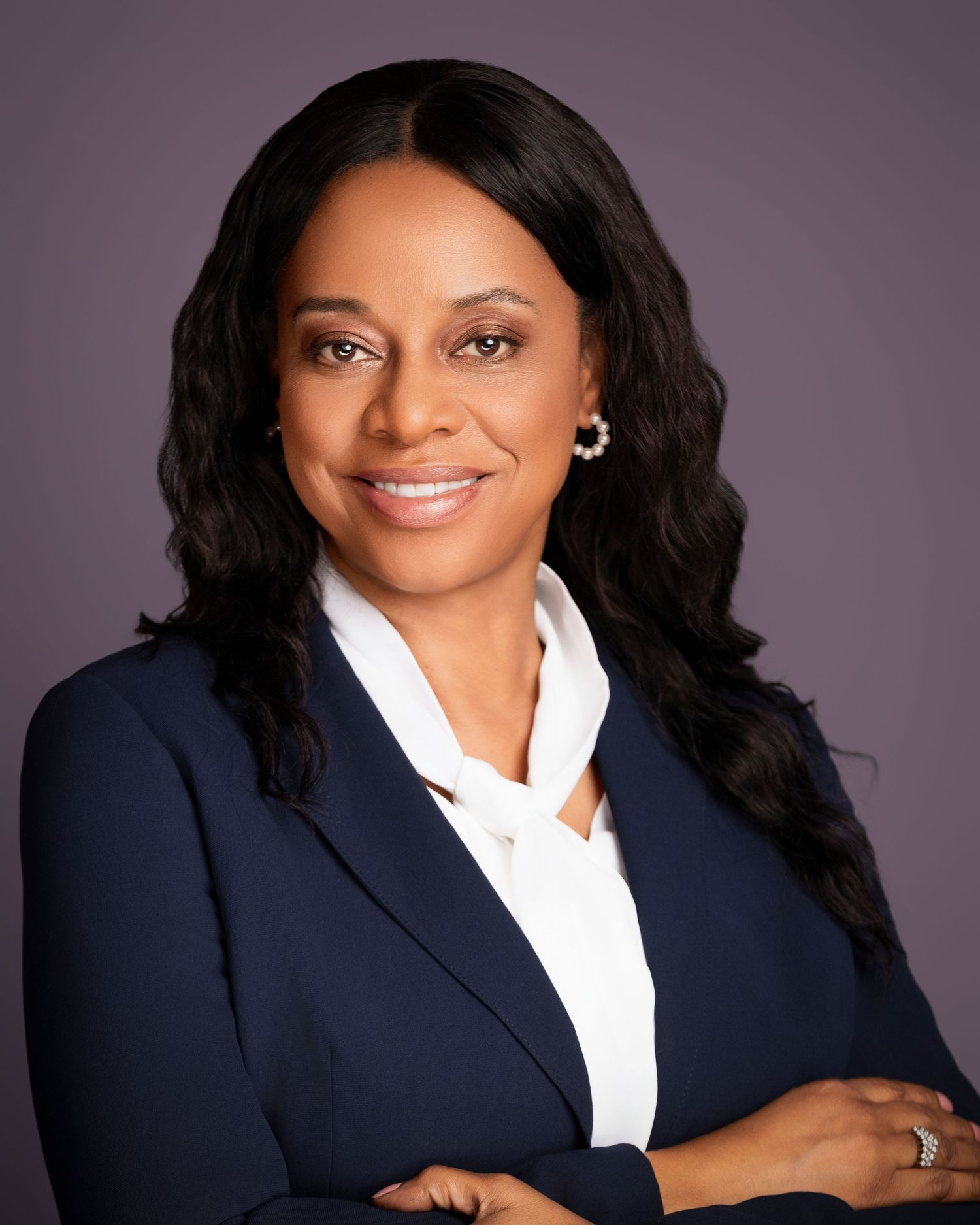 Executive portrait in navy blazer and white collar shirt against purple background.