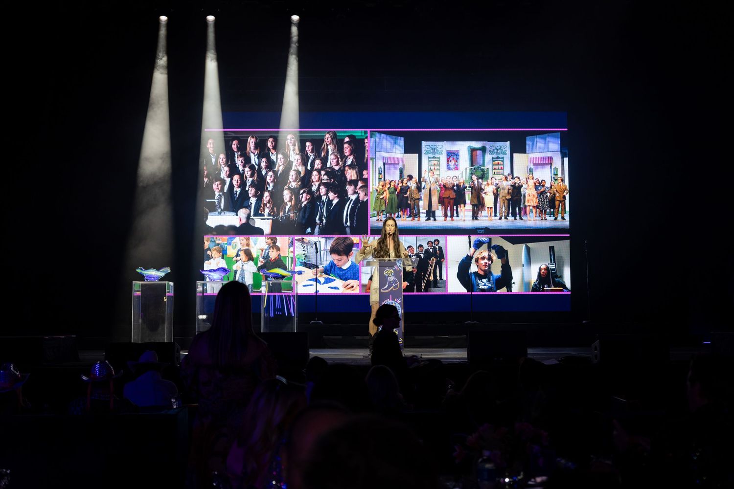 Concert stage with large video screens and spotlights illuminating a dark performance venue during a live show.