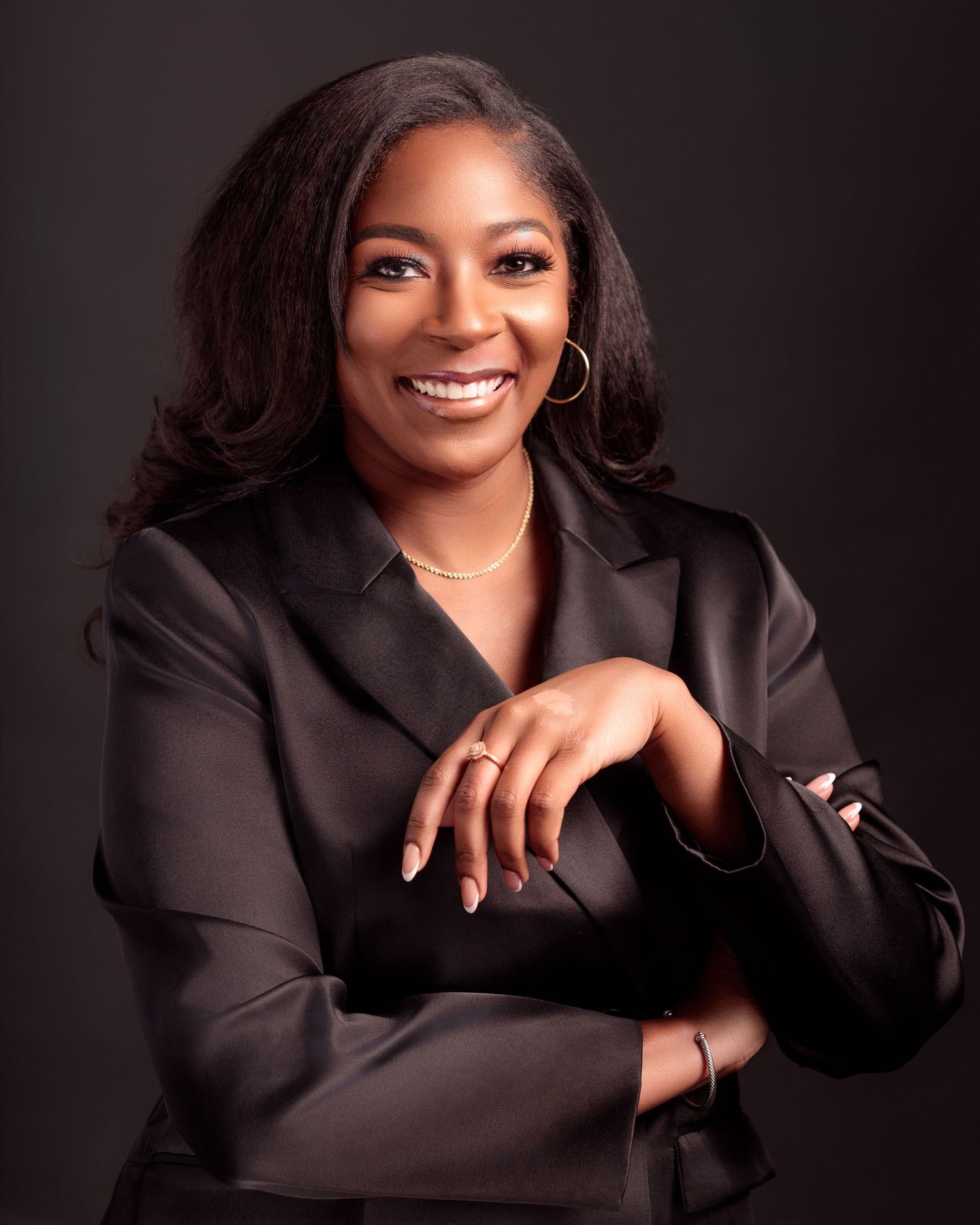 Professional studio portrait featuring elegant black blazer and warm smile against dark background.