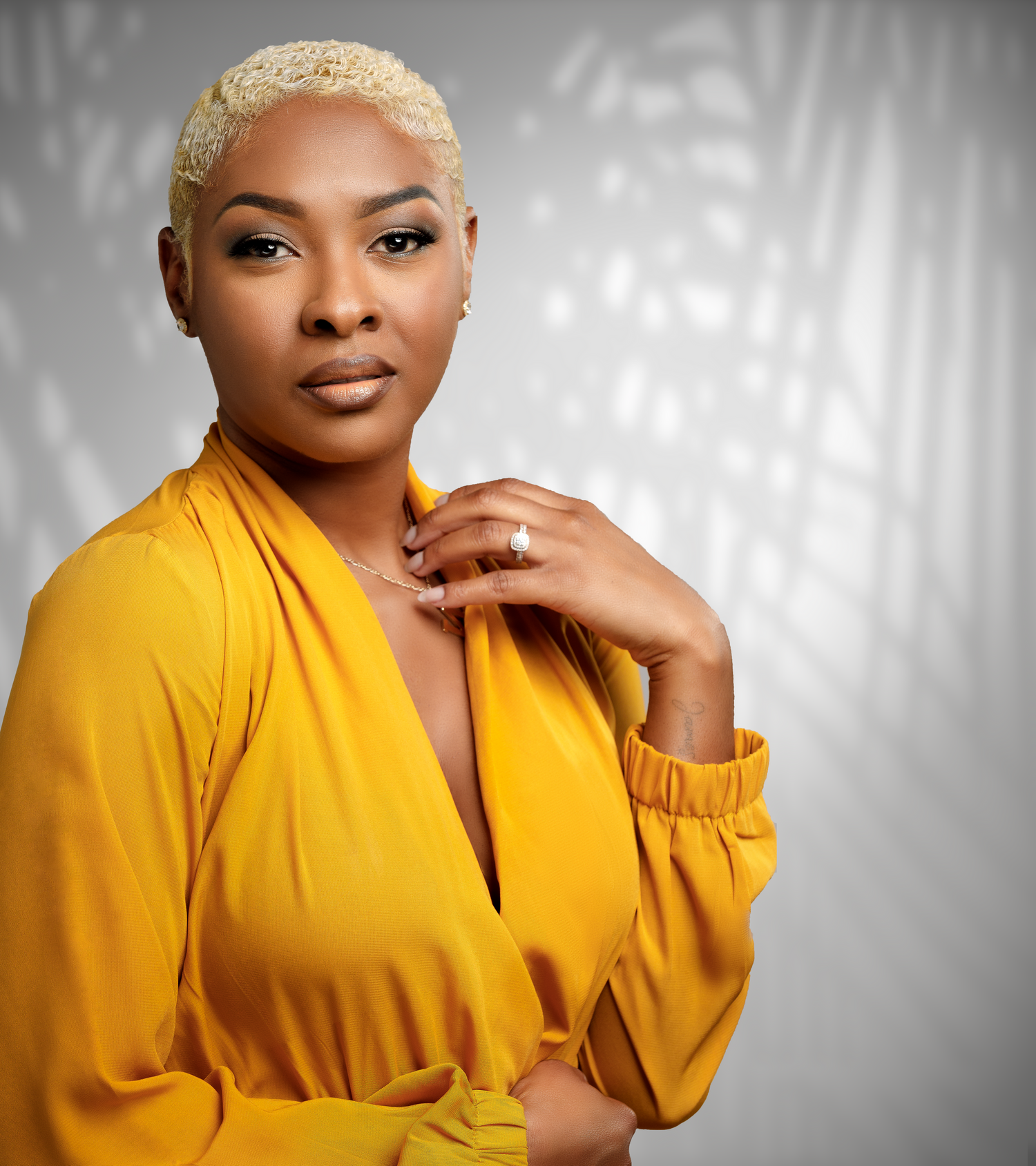 Professional studio portrait with yellow blouse against gray background.