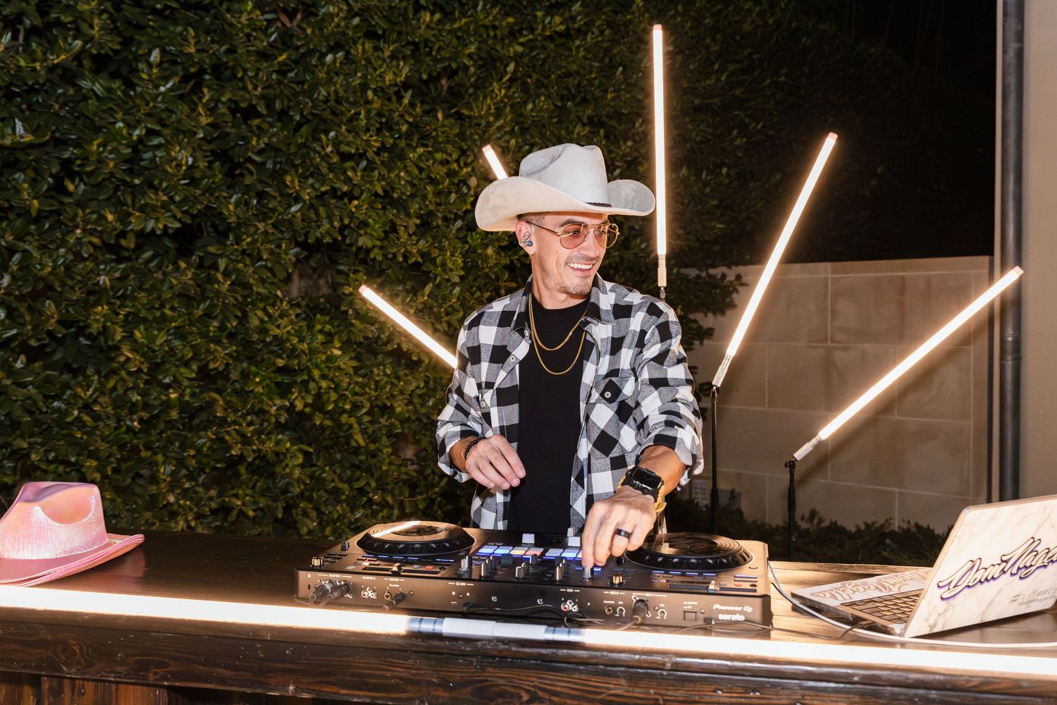 DJ performs at an outdoor venue with illuminated light fixtures creating an atmospheric ambiance.