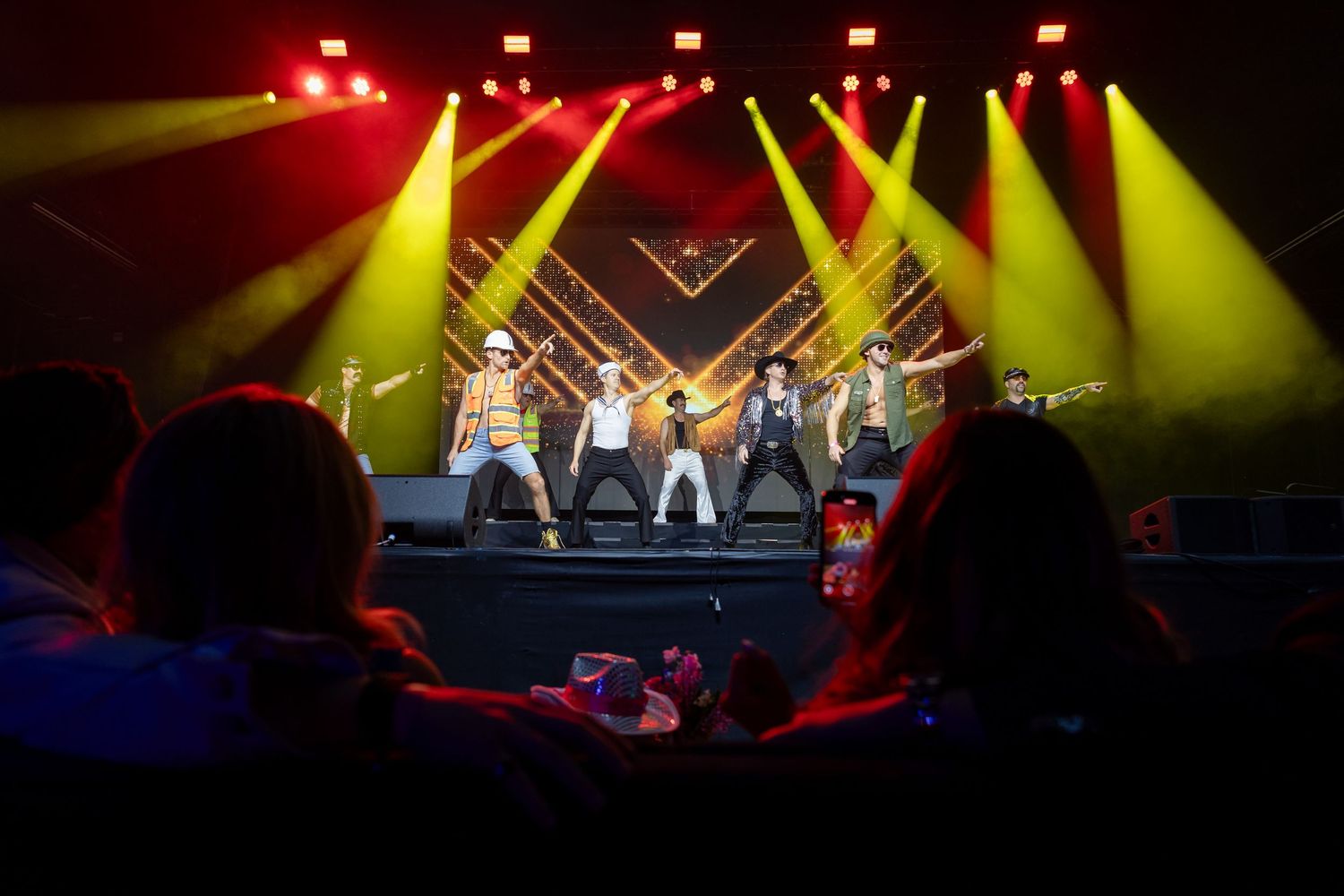 Concert performers on stage illuminated by dramatic red and yellow spotlights during a live music performance.