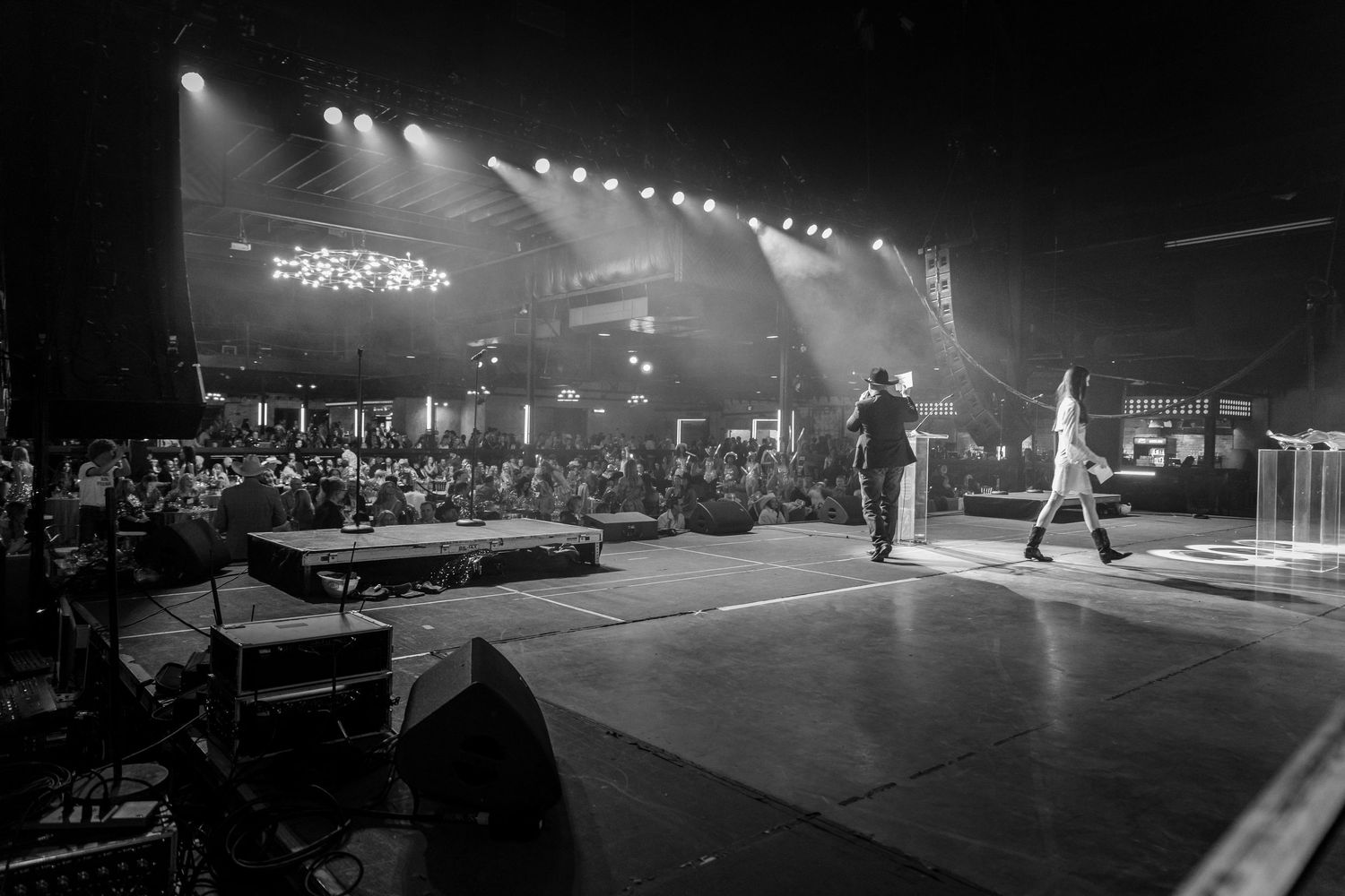 A black and white panoramic collage of concert stage lighting and performance scenes with dramatic spotlights.