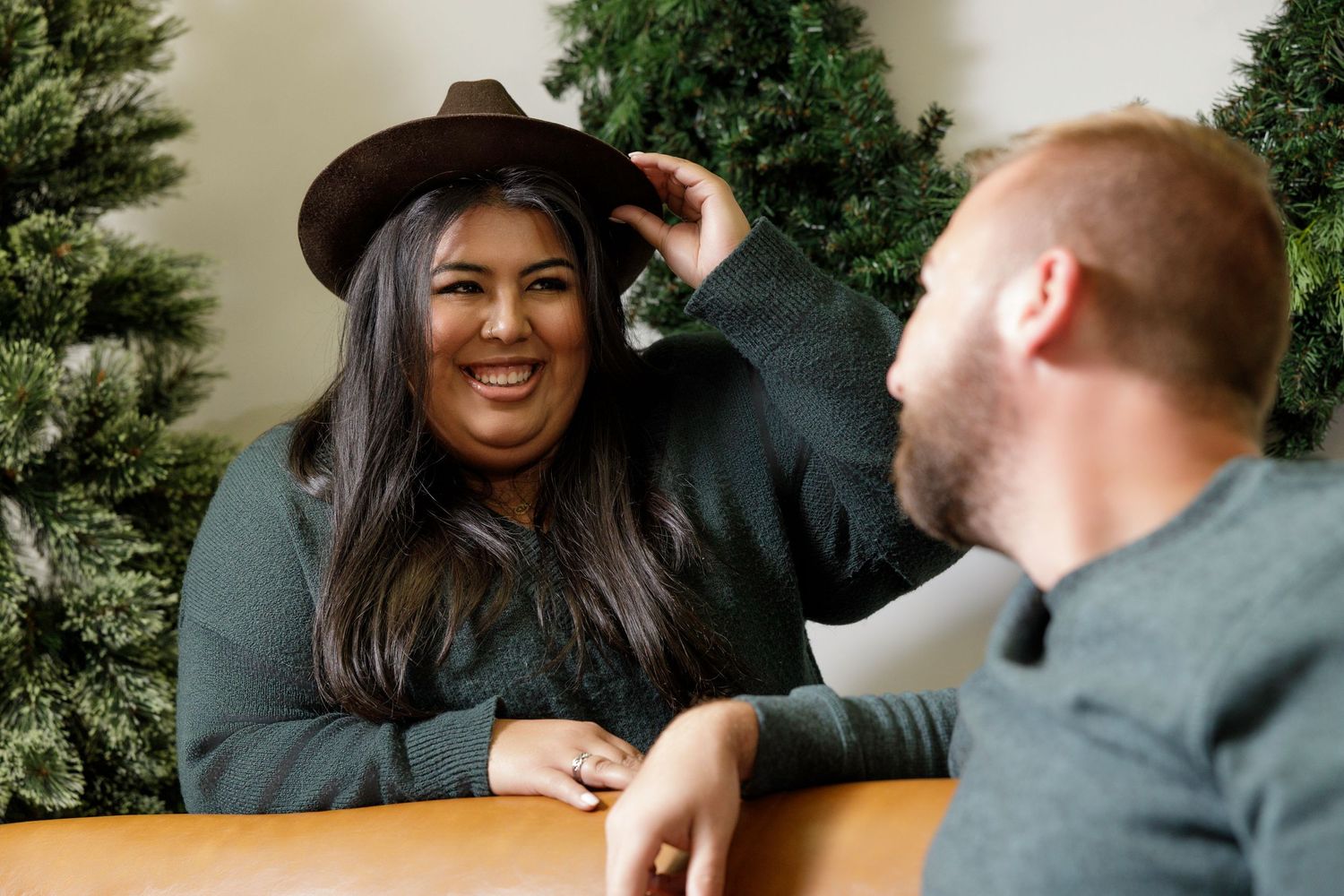 Indoor holiday photoshoot with couple exchanging gifts near Christmas trees.