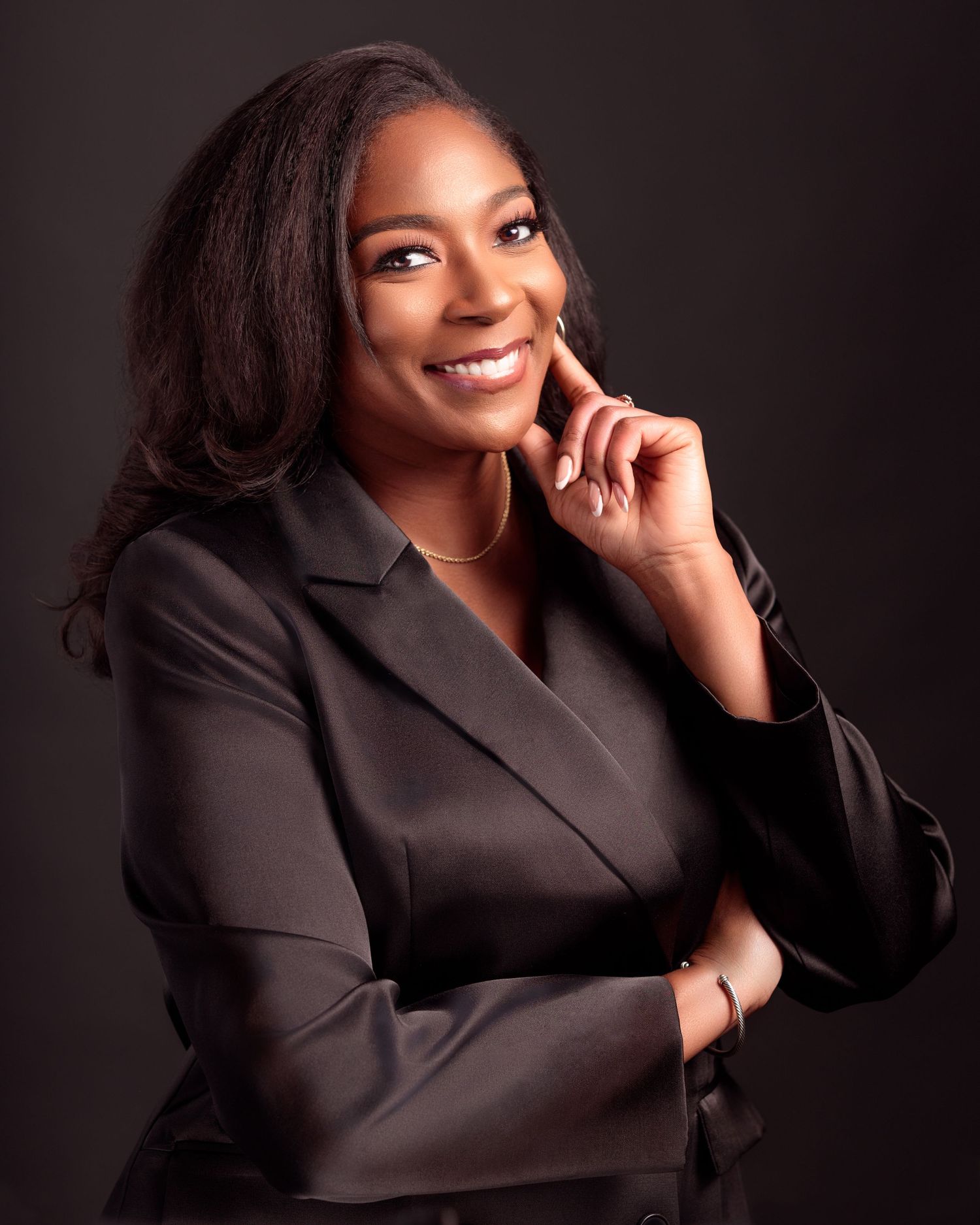 Elegant corporate headshot with black blazer and natural makeup against dark background.
