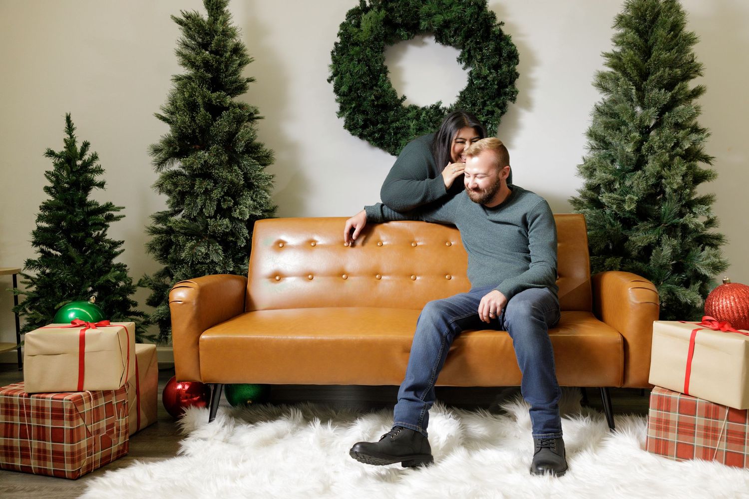 Cozy Christmas scene with evergreen trees, wreath, and wrapped gifts on brown leather couch.