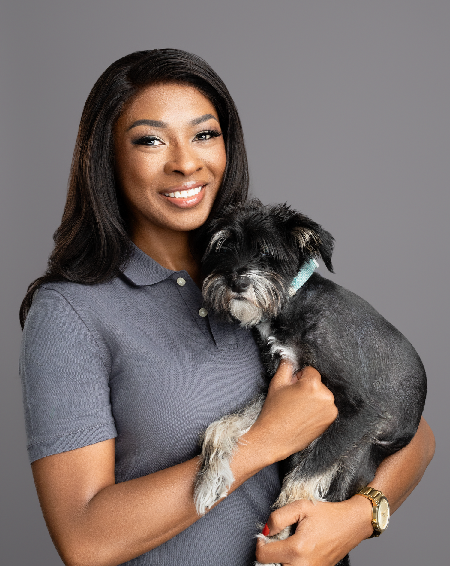 Grey polo-clad professional holding small black and white dog in studio portrait.