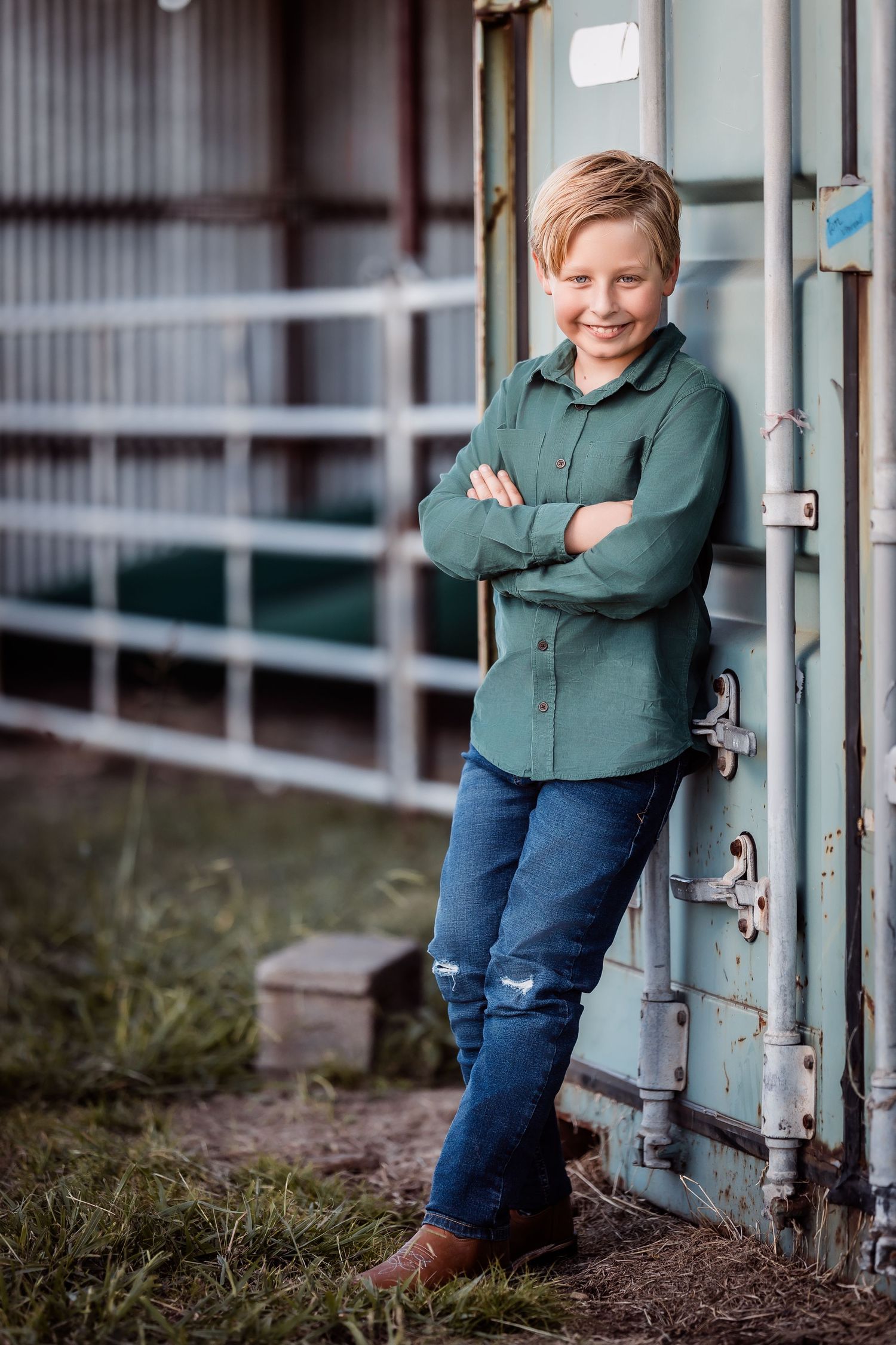 Child in green hoodie and jeans posing casually against metal gate outdoors.