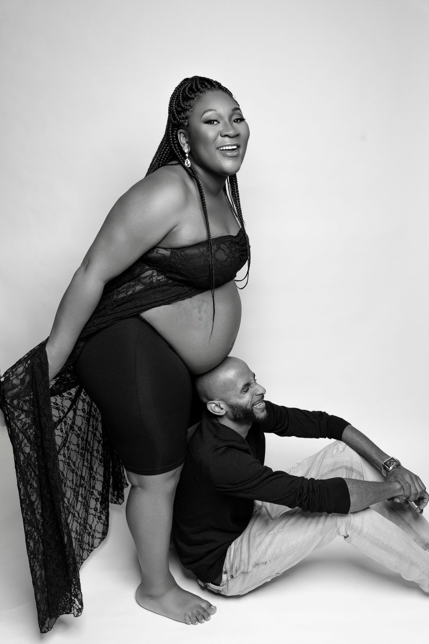 Black and white maternity photo showing a couple posing together, with flowing lace fabric adding elegance to the shot.