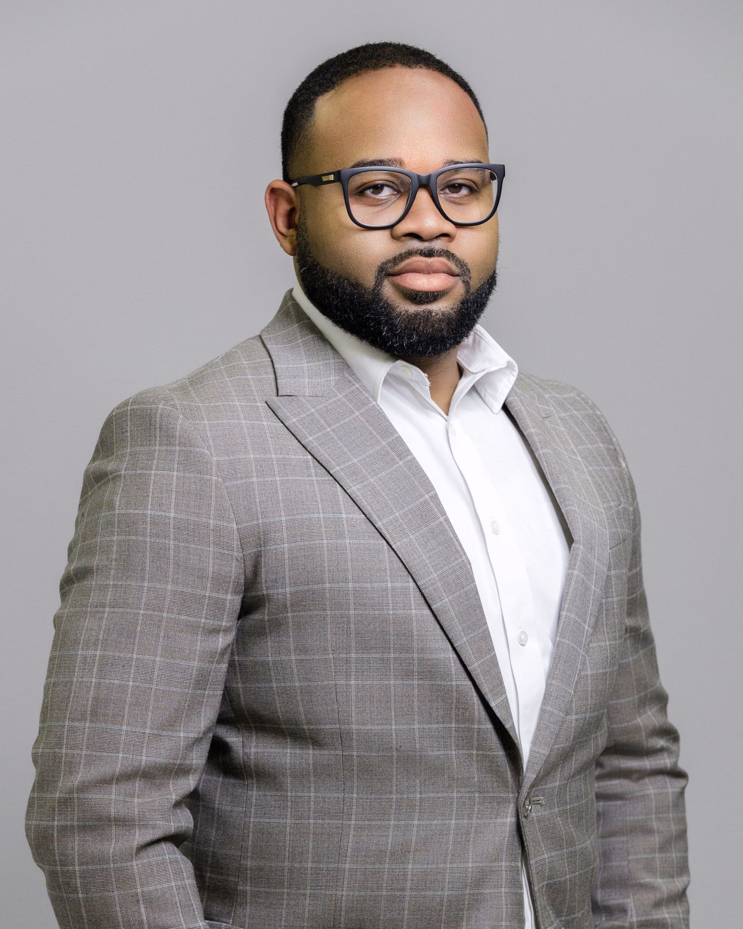 Man in checkered grey suit and glasses poses professionally against grey background.