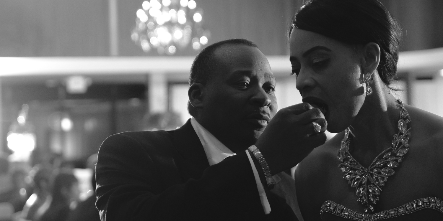 A black and white photograph shows two people in formal attire having an intimate conversation at an elegant event.