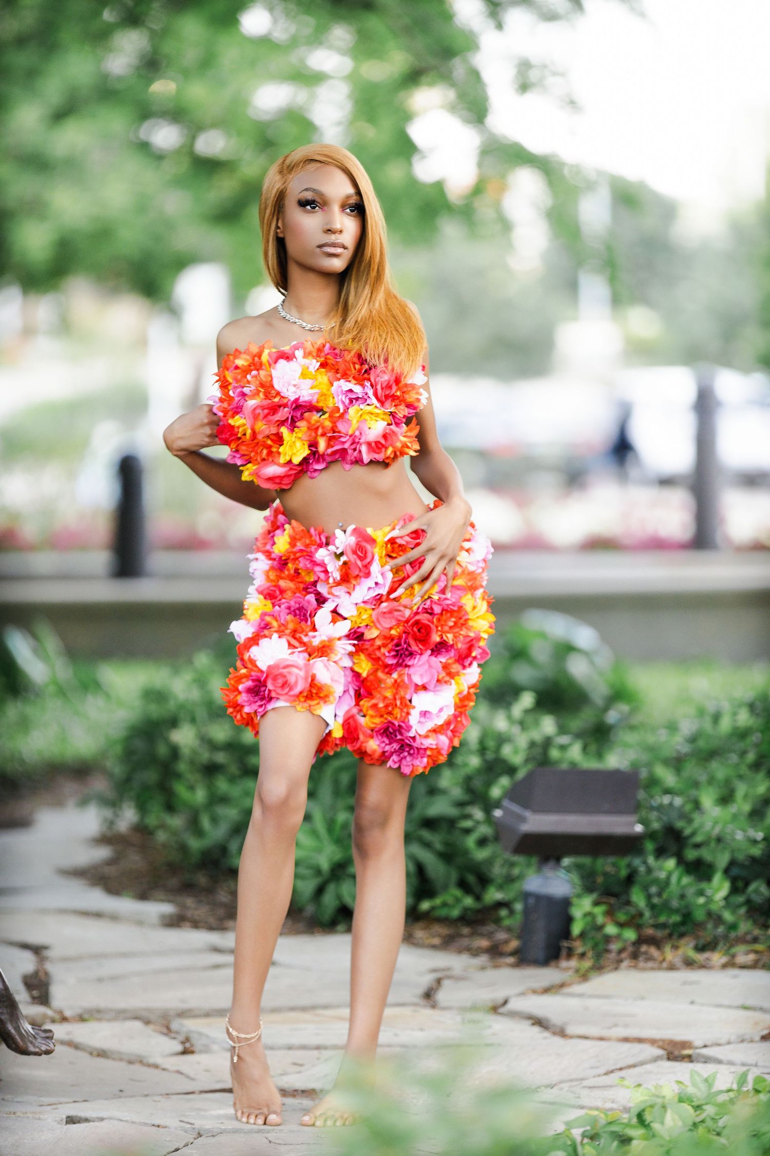 Outdoor fashion photography with tropical floral elements and stone pathway details.