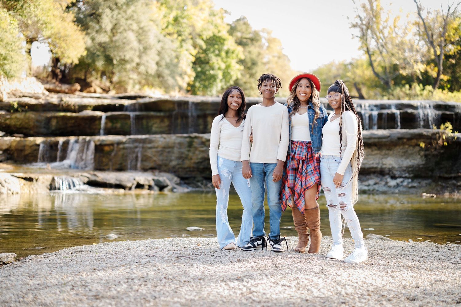 Family photoshoot by a scenic waterfall with everyone wearing coordinated white and denim outfits.