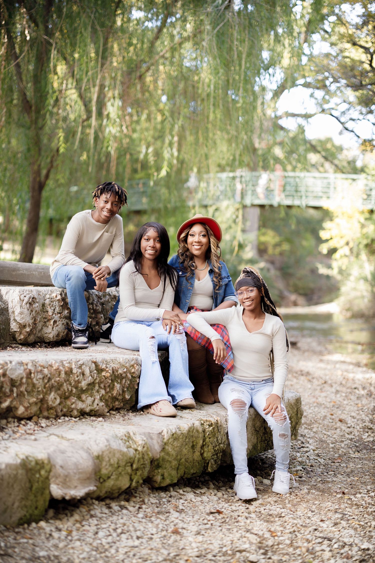 Group relaxing on stone wall under willow trees during outdoor photo session.
