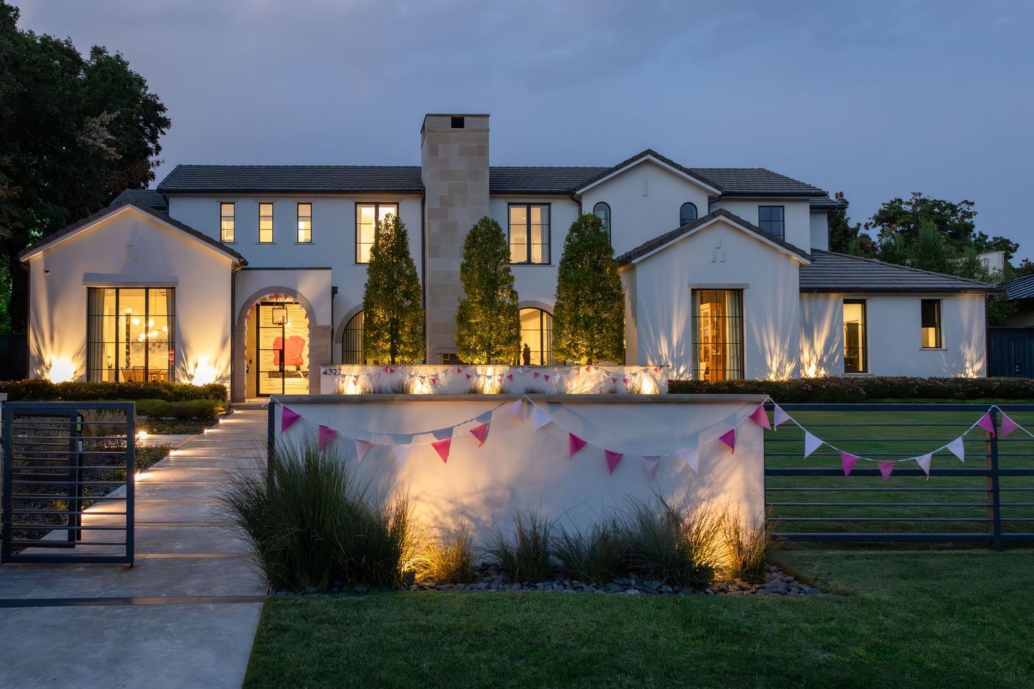 Modern white wedding venue illuminated at dusk with warm glowing windows and landscaped grounds.