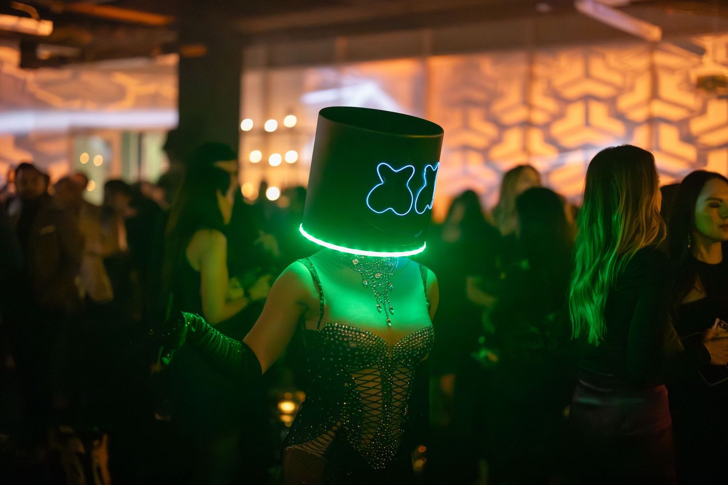 A crowded nightclub dance floor illuminated with green lighting and silhouettes of people dancing.