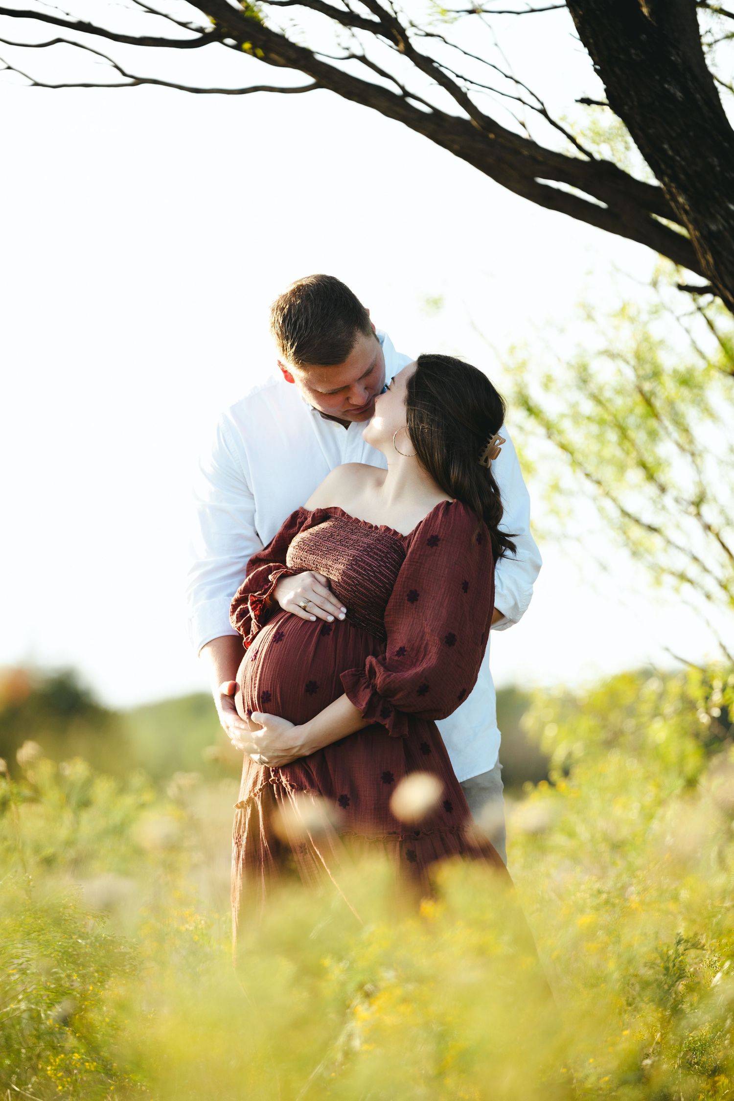 Intimate couple portrait in a field with soft sunlight filtering through trees.