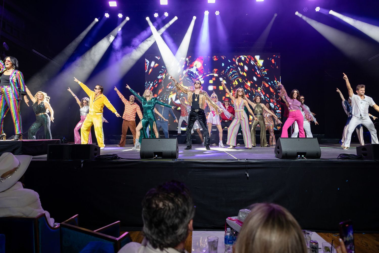Performers dance and entertain on a brightly lit stage during a dynamic concert production with purple lighting effects.