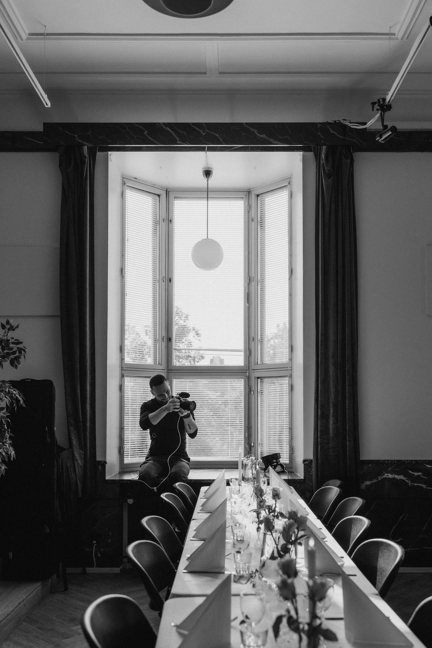 Wedding videographer documenting reception setup in elegant historic venue with large window light