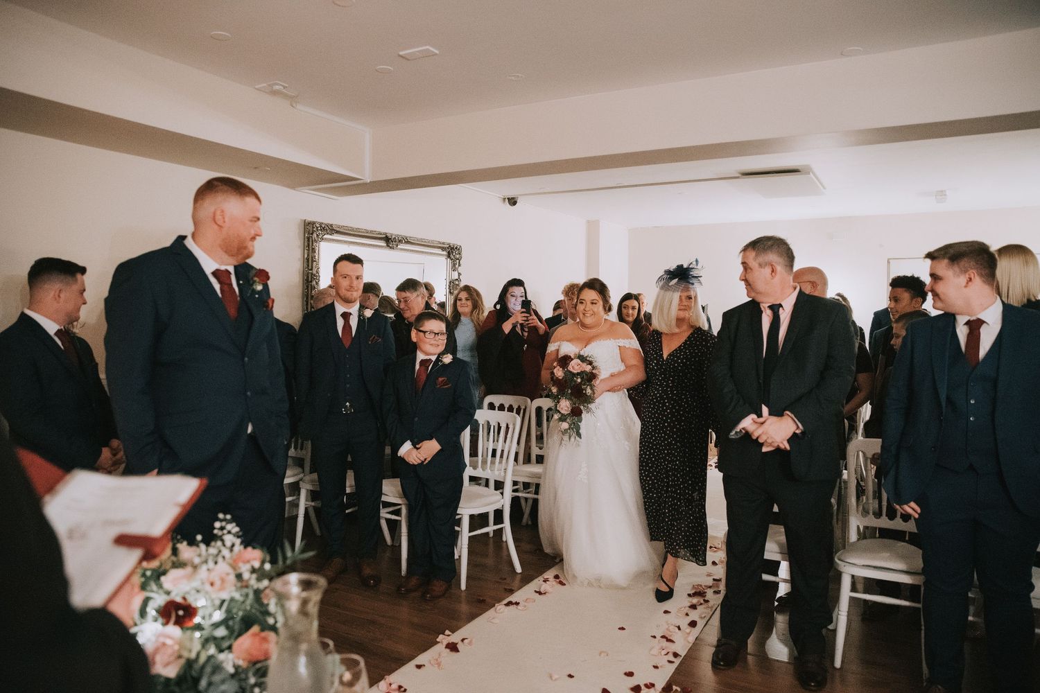 Bride walks down the aisle at an elegant indoor wedding ceremony with guests and groom waiting at the altar.