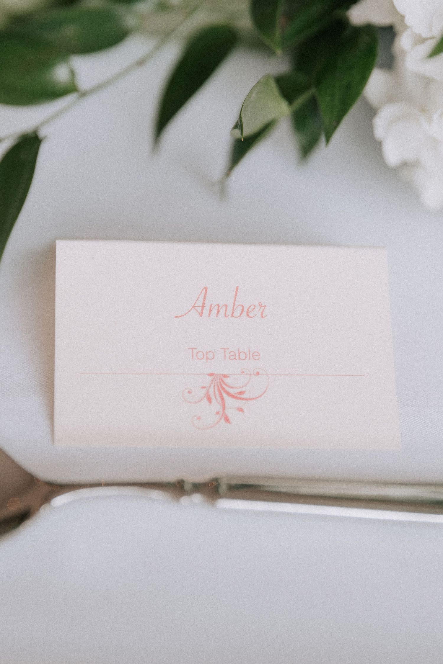 Elegant wedding place card for Amber at the Top Table, featuring pink script font and decorative flourish on cream cardstock.