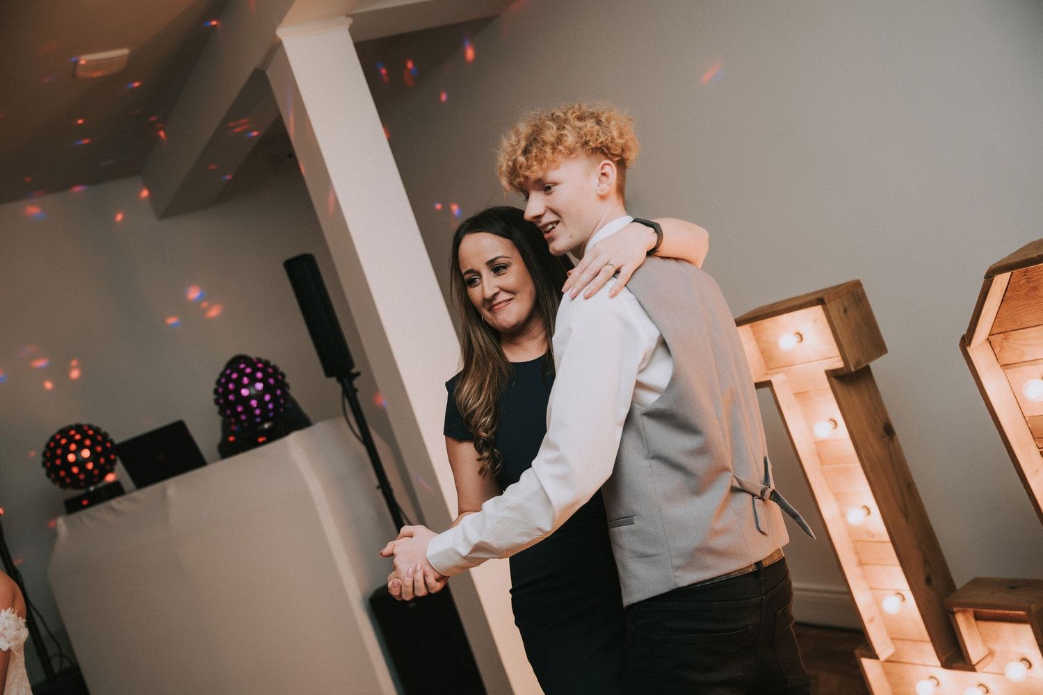 Couple dancing together at a wedding reception with disco lights glowing in the background.