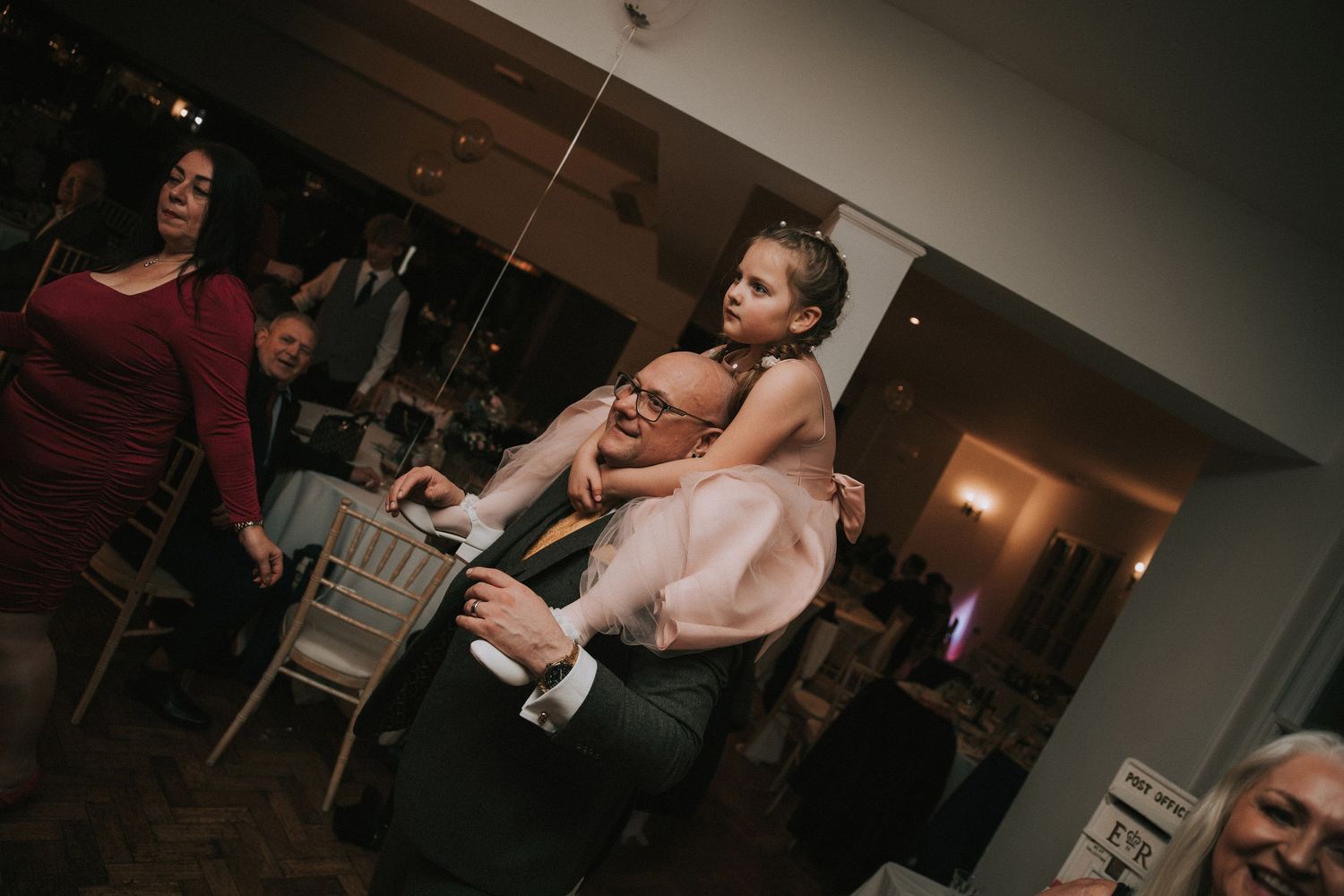 Guest carrying a child on their back during lively wedding reception dance floor celebration indoors.