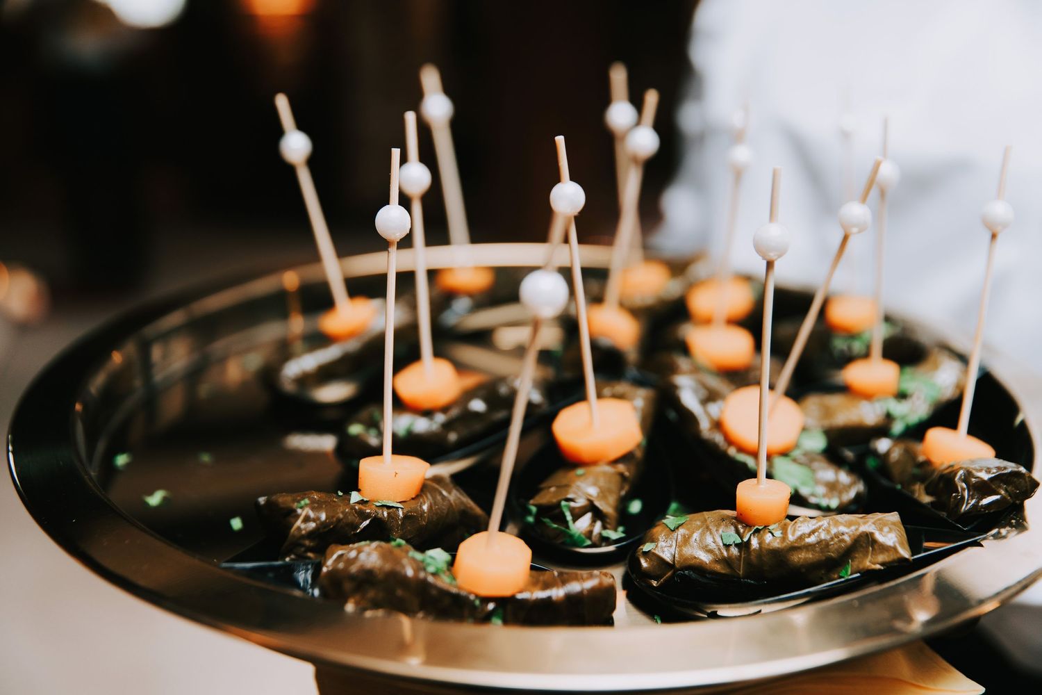 Elegant appetizer tray with stuffed grape leaves topped with orange garnish and decorative picks at a catered event.