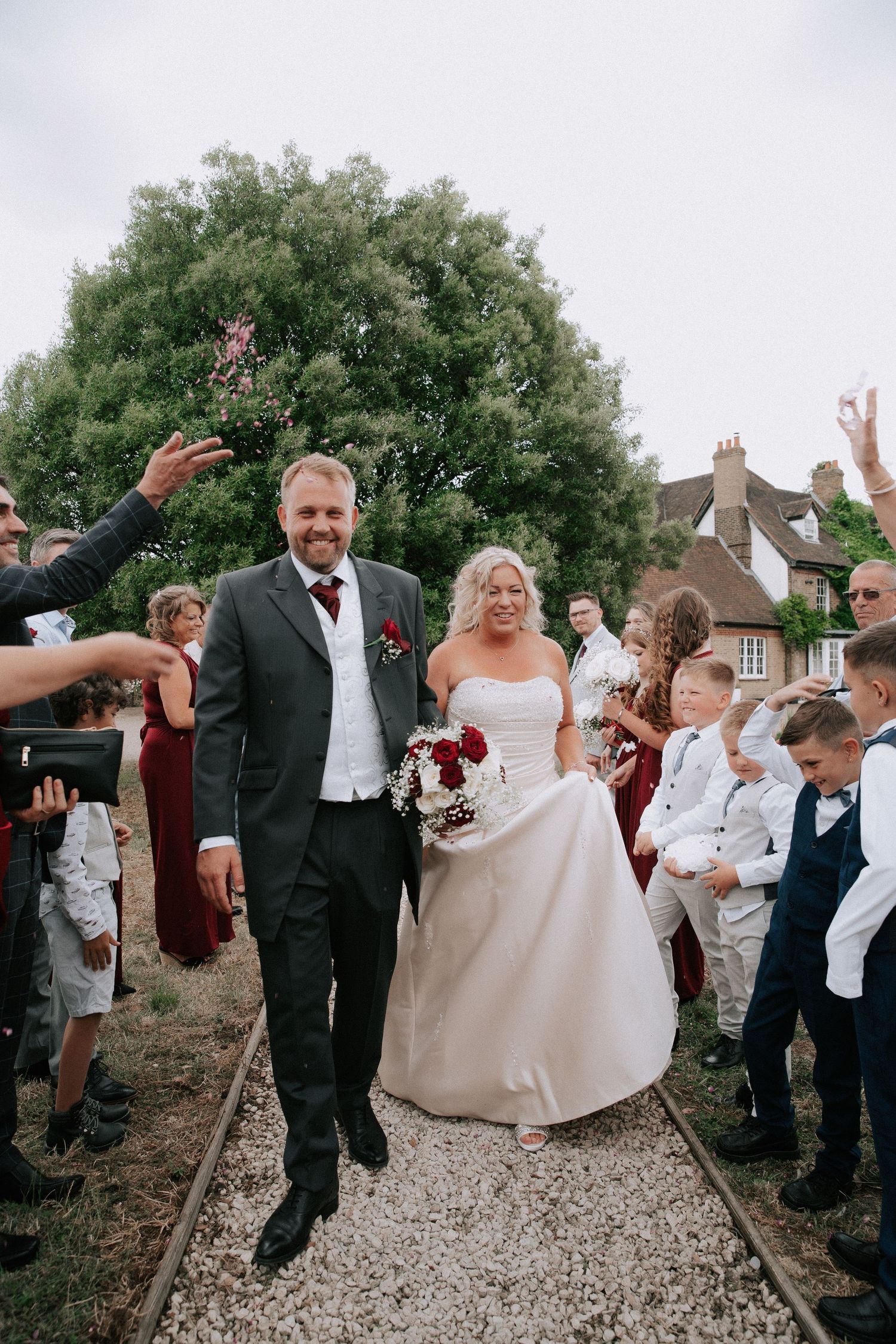 Newlyweds walk through confetti shower as smiling guests celebrate their outdoor wedding ceremony.