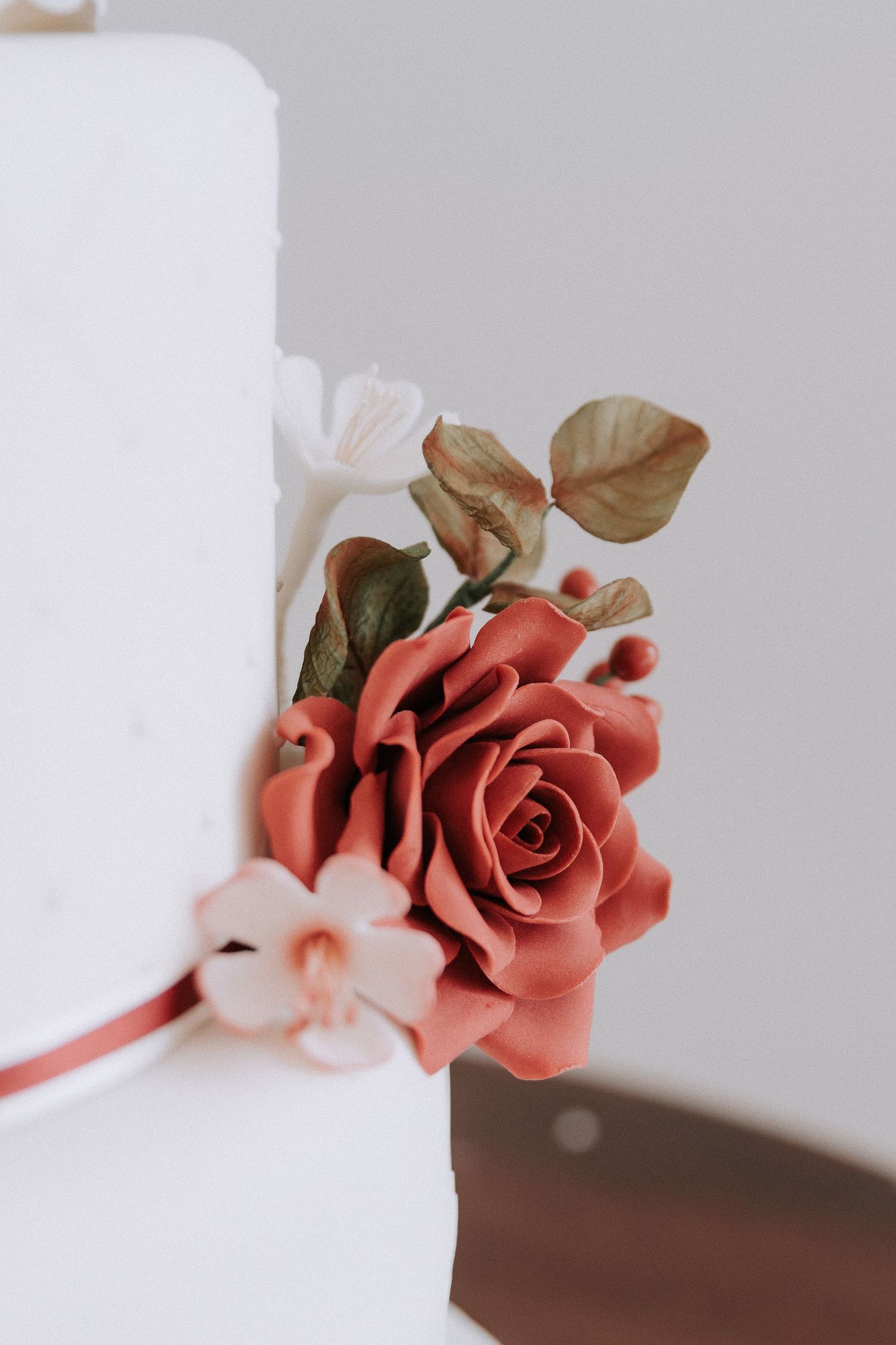 Elegant white wedding cake decorated with a terracotta sugar rose and delicate floral accents.