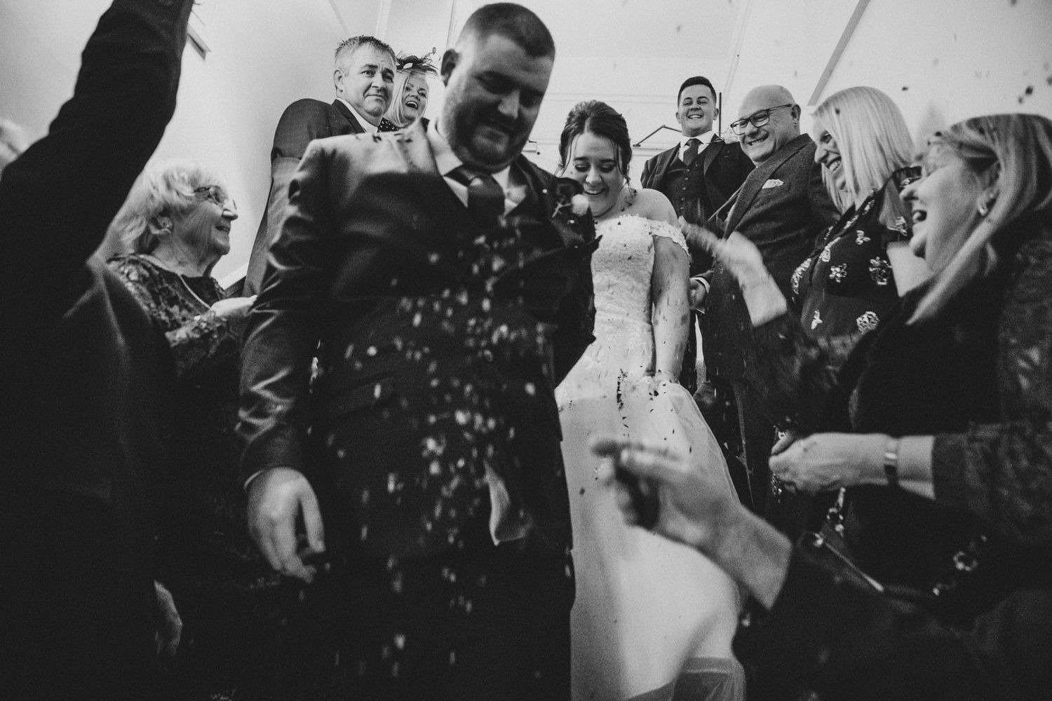 Black and white photo of wedding guests throwing confetti over the bride and groom.