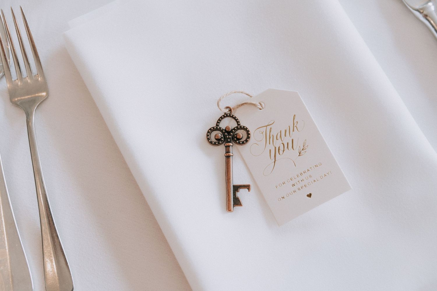 Elegant wedding favor with vintage skeleton key bottle opener and thank you tag on white linen napkin.
