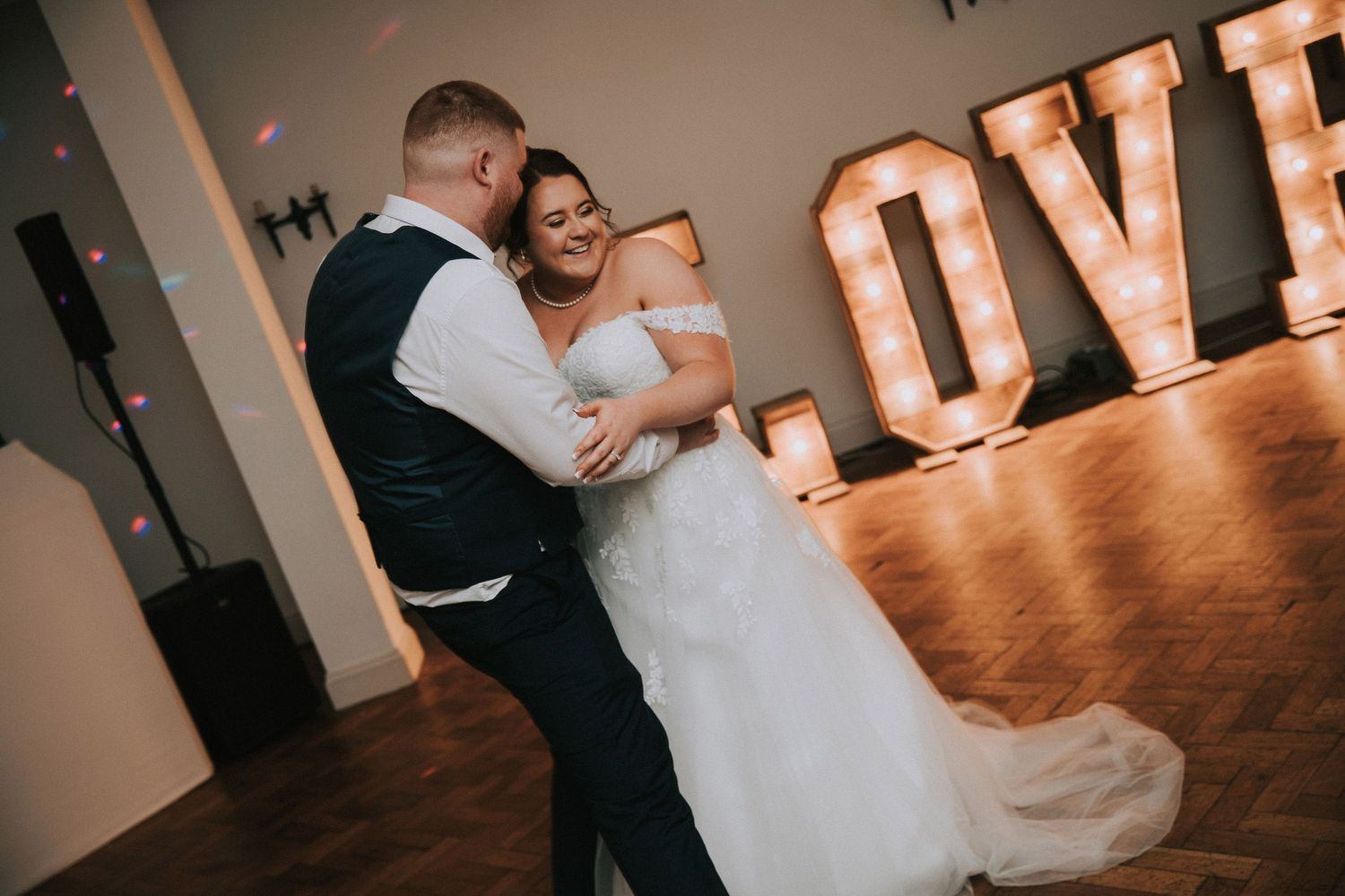 Bride and groom share their first dance in front of illuminated LOVE letters at their wedding reception.