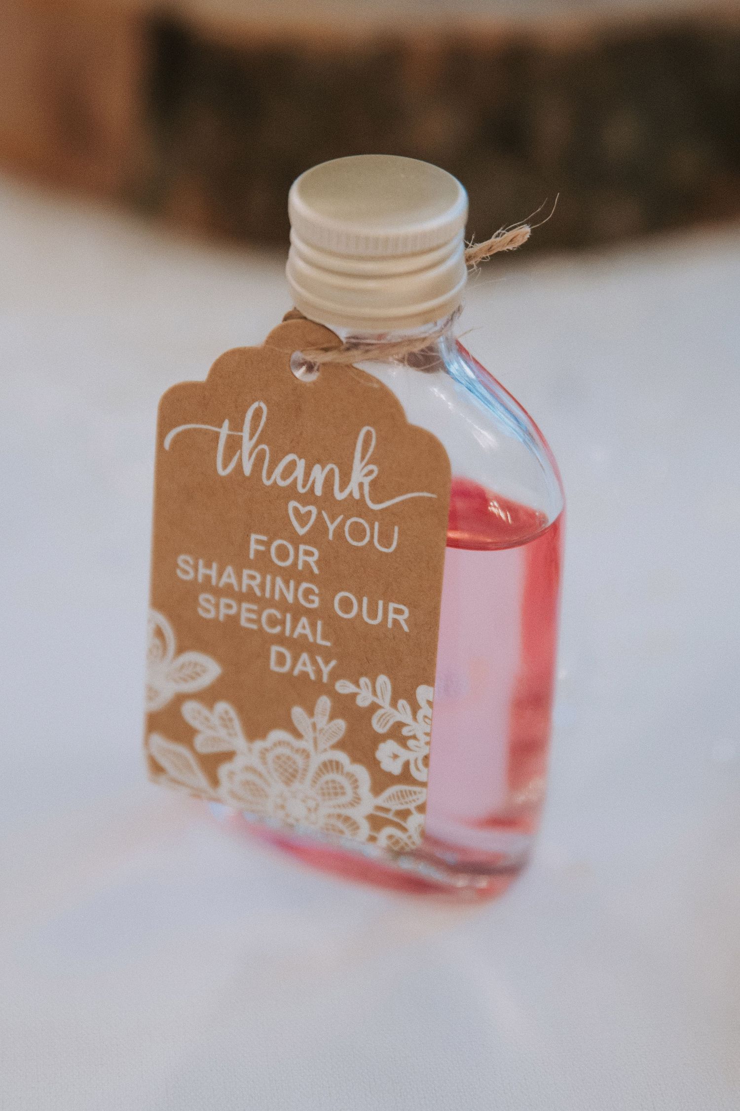 Wedding favor mini bottle with thank you tag reading sharing our special day on white surface.