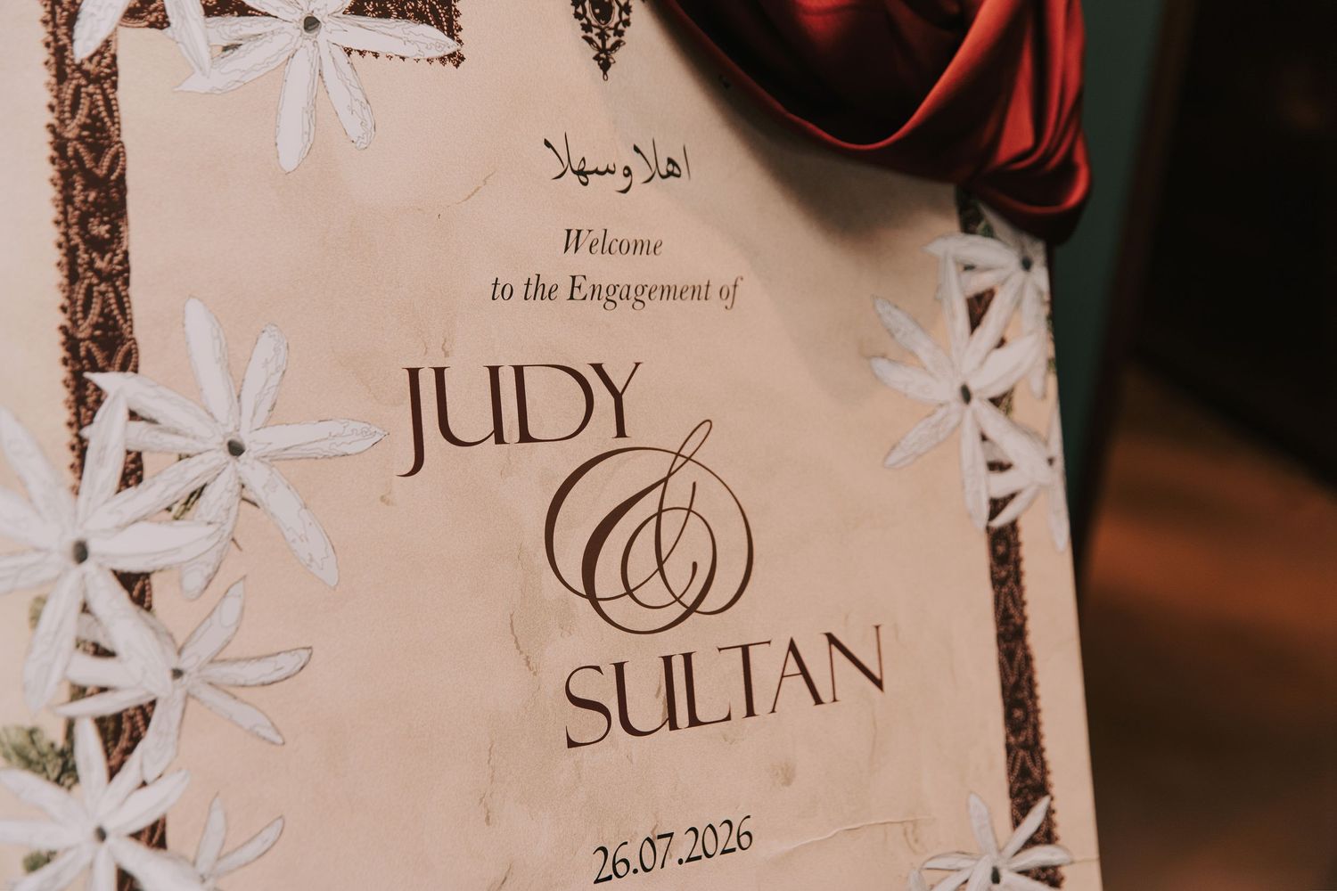 Elegant engagement welcome sign for Judy and Sultan, dated 26.07.2026, with floral decorations and Arabic calligraphy.
