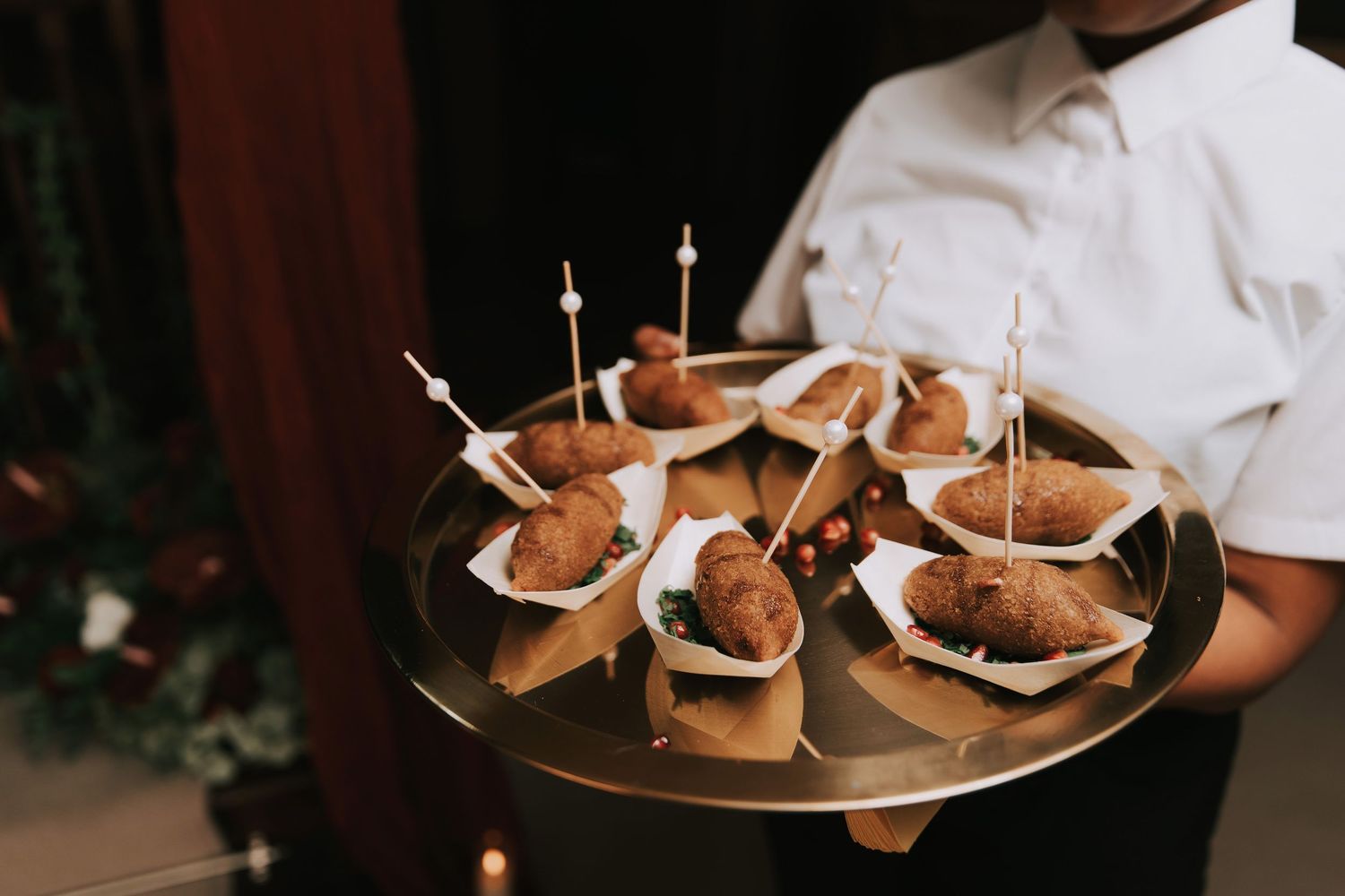 Waiter holding a gold tray of elegant appetizers in paper cones with decorative candles at a catered event.