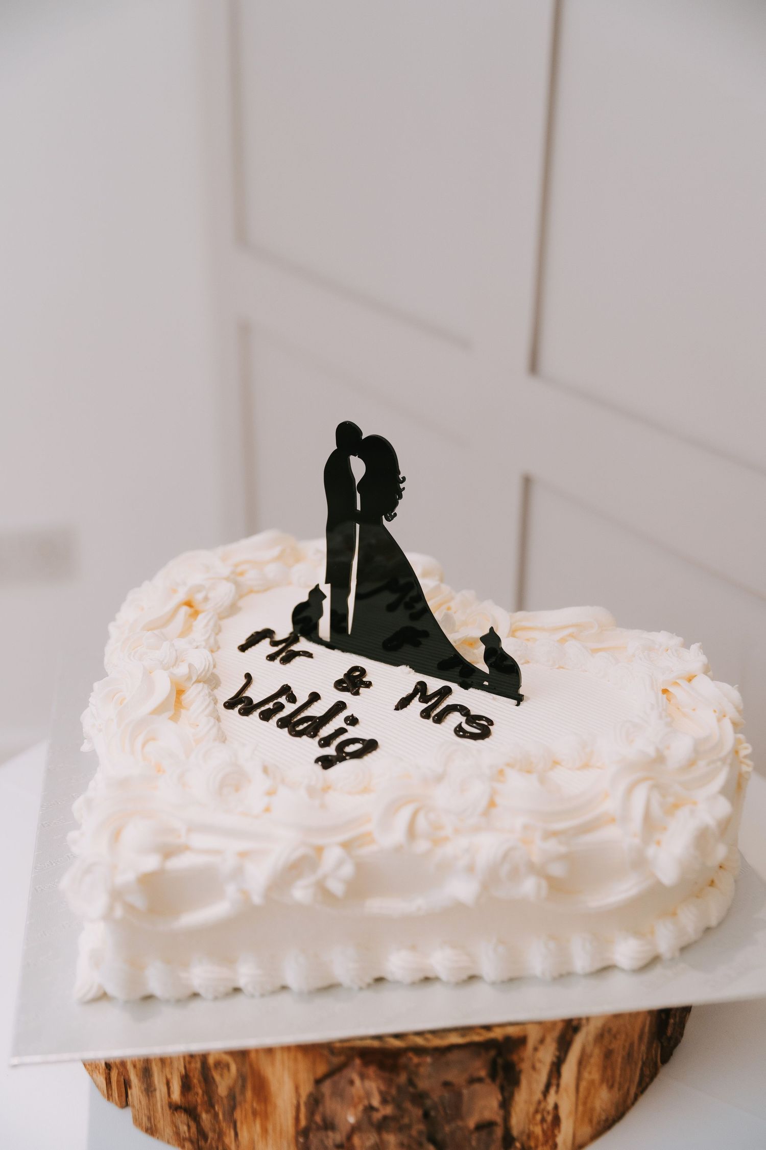 Heart-shaped white wedding cake with Mr & Mrs Wildig inscription and silhouette couple topper on rustic wood stand - Ye Olde Plough House