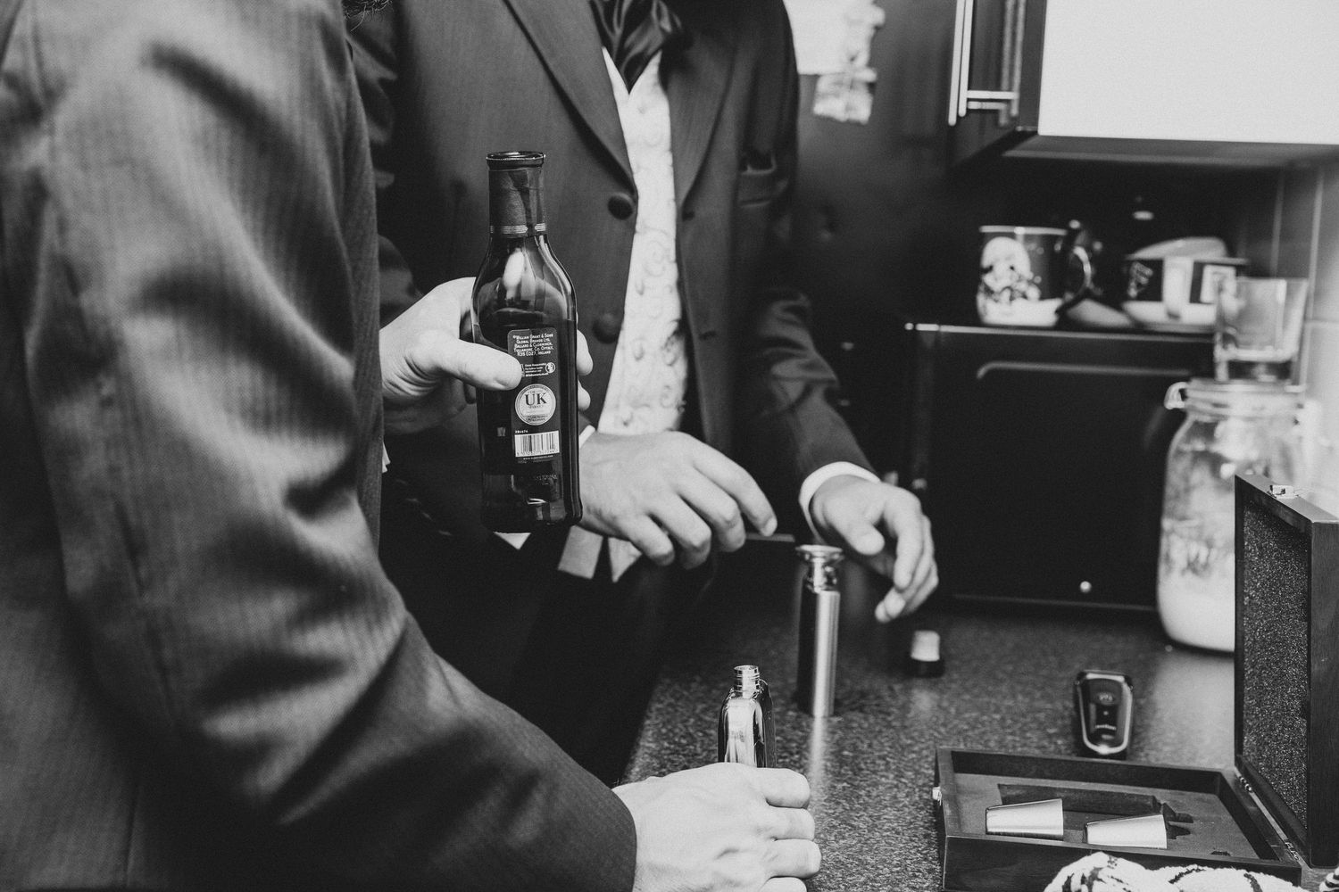 Black and white photo of two men in suits holding beer bottles at a bar counter.